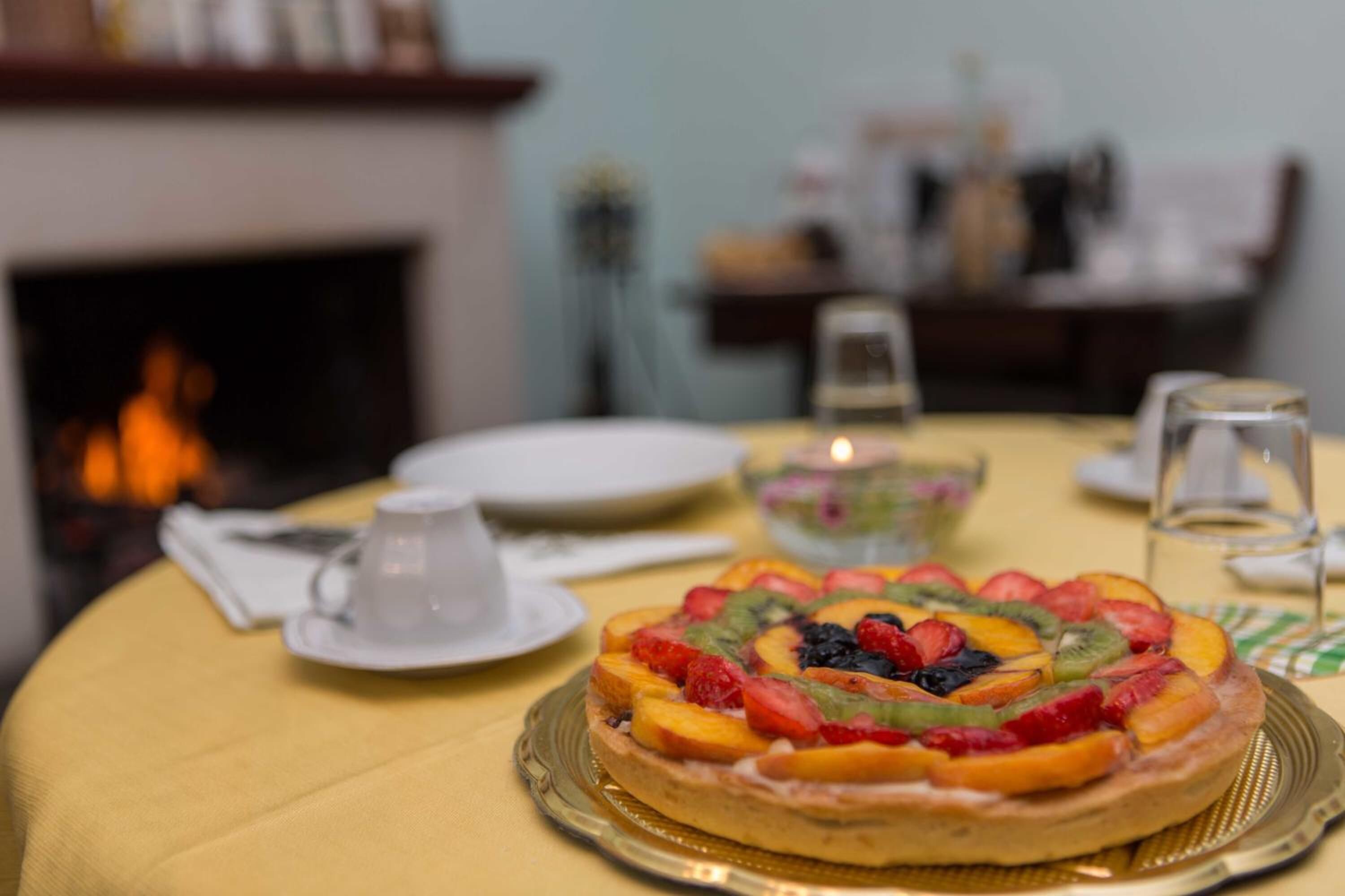 Una tarta de frutas sobre una mesa con mantel amarillo, rodeada de platos, un vaso y una vela.