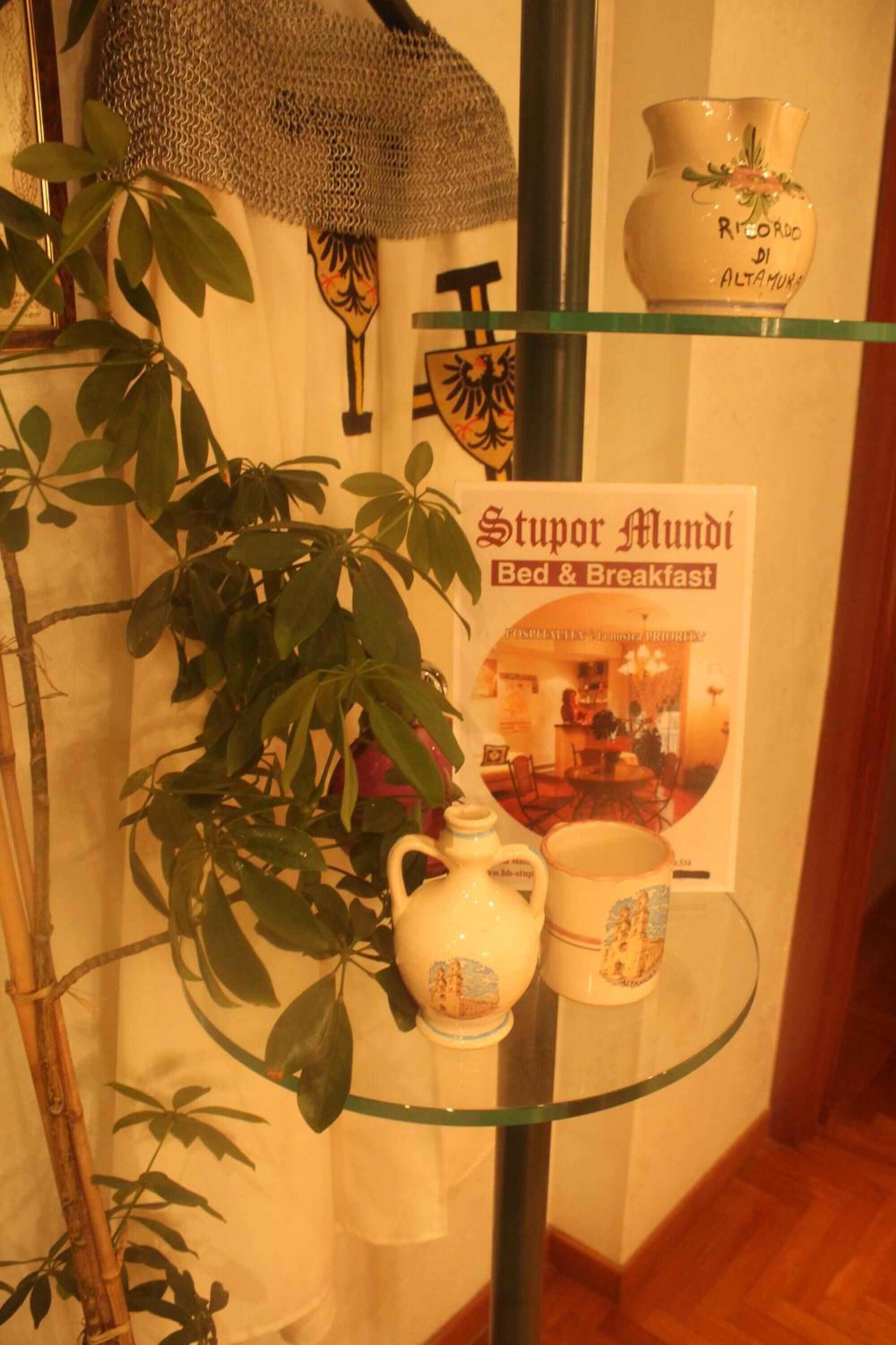 Uma mesa de vidro com um livro intitulado 'Stupor Mundi Bed & Breakfast' e um vaso decorativo.