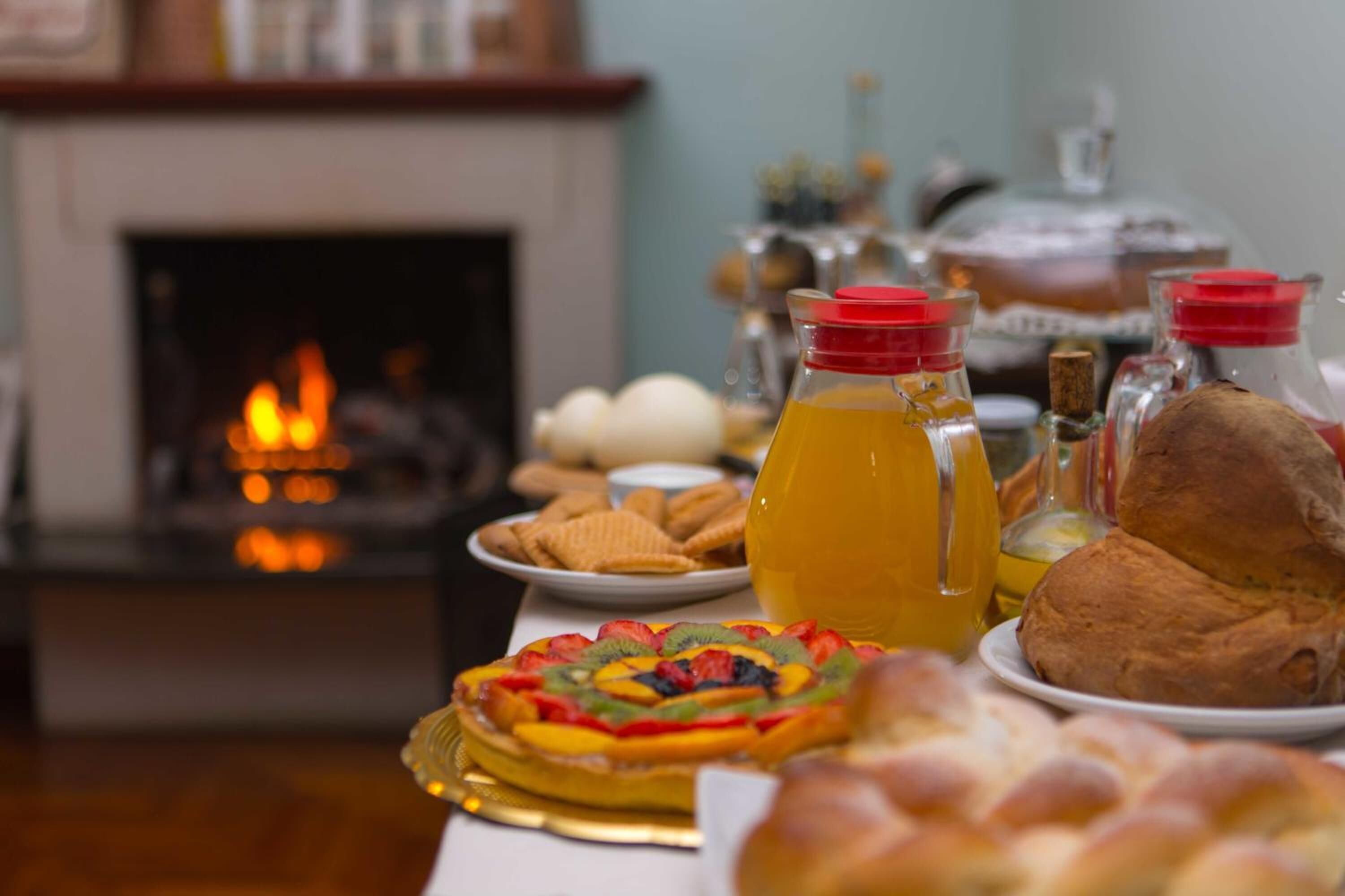 Una mesa con una tarta de frutas, pan y botellas de jugo en una habitación con una chimenea al fondo.