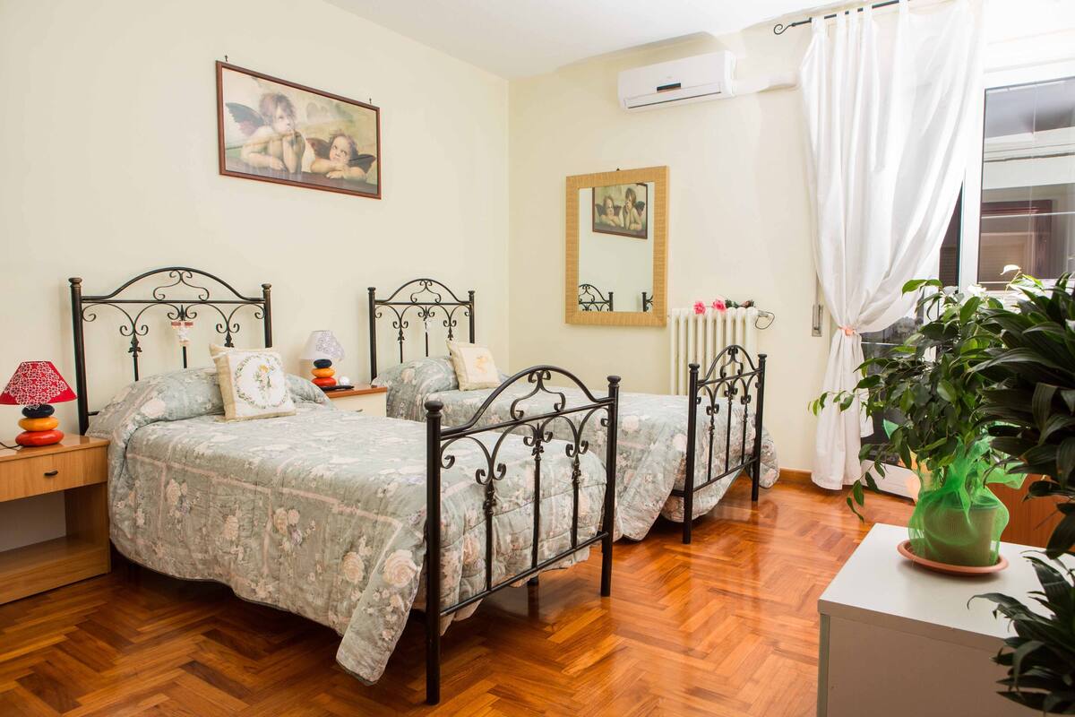 A bedroom with two beds, a wooden floor, a radiator, and a window with curtains.