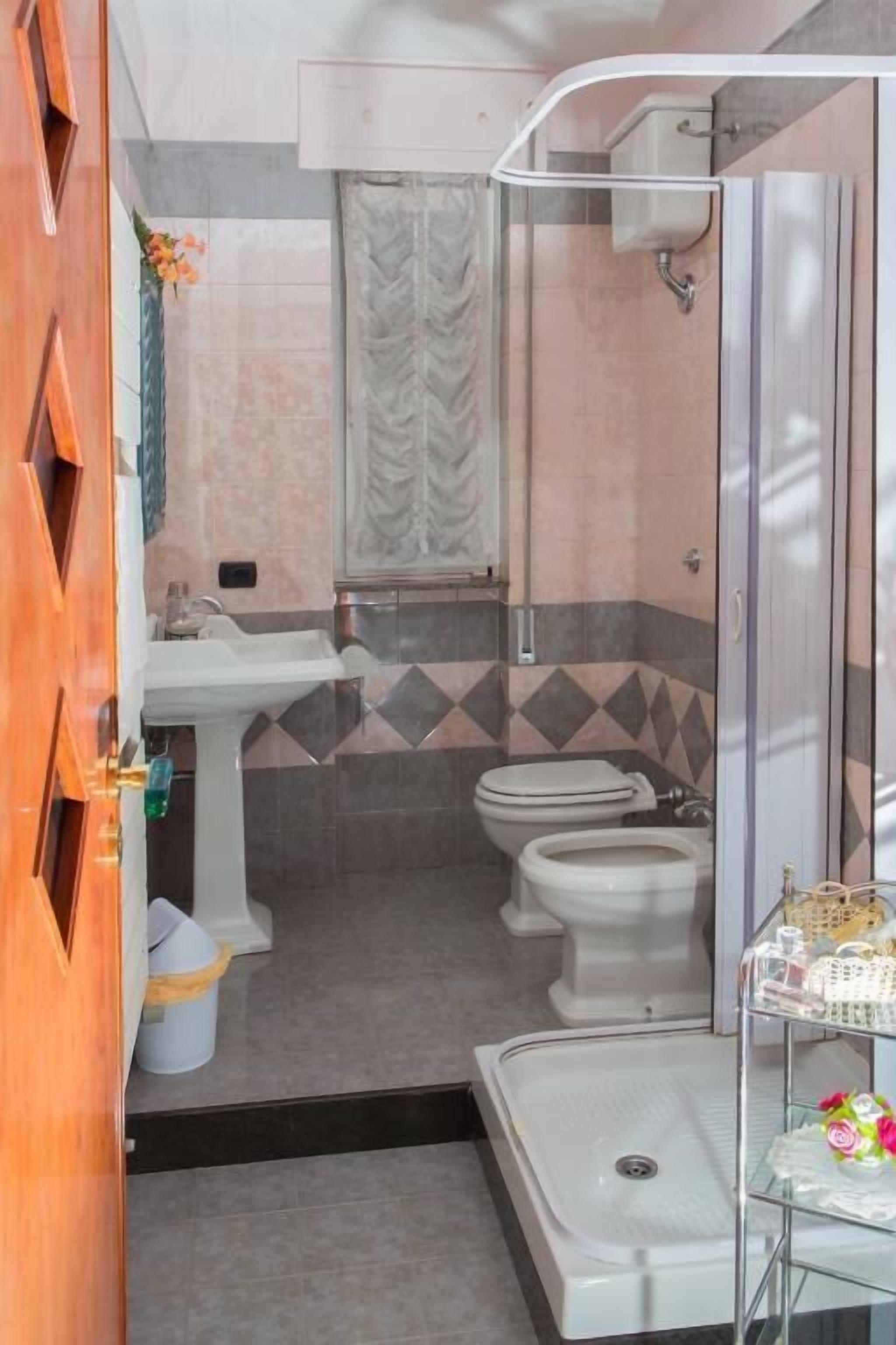 A compact bathroom with a shower, two toilets, and a sink.