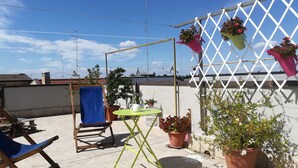 A rooftop terrace with a wooden chair, a small table, potted plants, and a white lattice structure. - Stupor Mundi (Altamura)