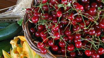 A wicker basket filled with cherries, a cucumber, and some flowers on a wooden table.