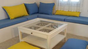 A room with a blue sofa set, a glass-top coffee table with a drawer, and yellow and blue cushions. - Theros Villa (Santorini)