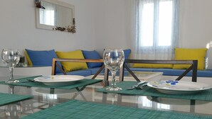 A dining area with a glass table, green placemats, and two wine glasses. - Theros Villa (Santorini)