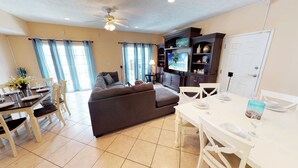 A well-lit living room with a sofa, dining table, and TV. - Myrtle Beach Villas 302A - 6 Bedroom Condo (Myrtle Beach)