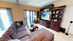 A living room with a large flat-screen TV, a sofa, a coffee table, and a cabinet with decorative items. - Myrtle Beach Villas 302A - 6 Bedroom Condo (Myrtle Beach)