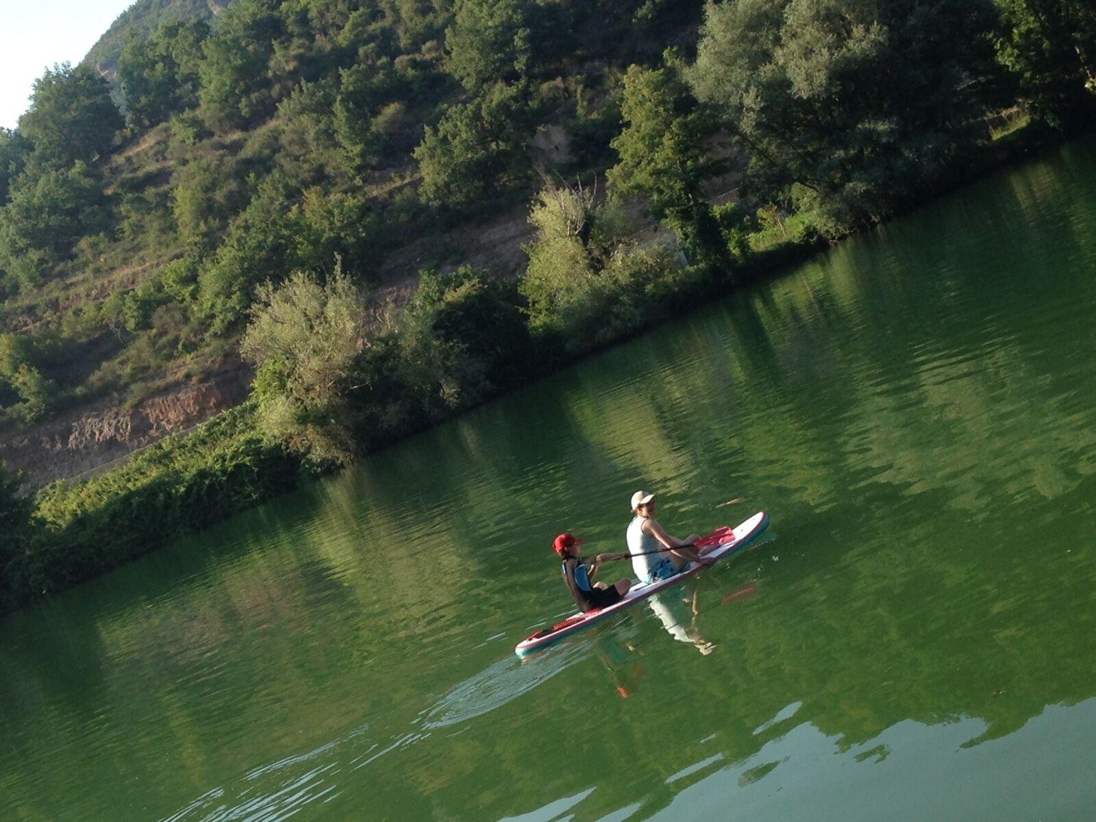 Una persona remando un canoa en un río tranquilo rodeado de abundante vegetación.