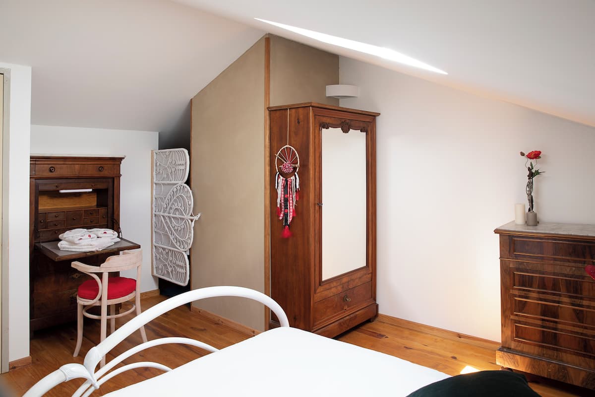 A bedroom with a wooden wardrobe, a desk with a chair, and a bed.