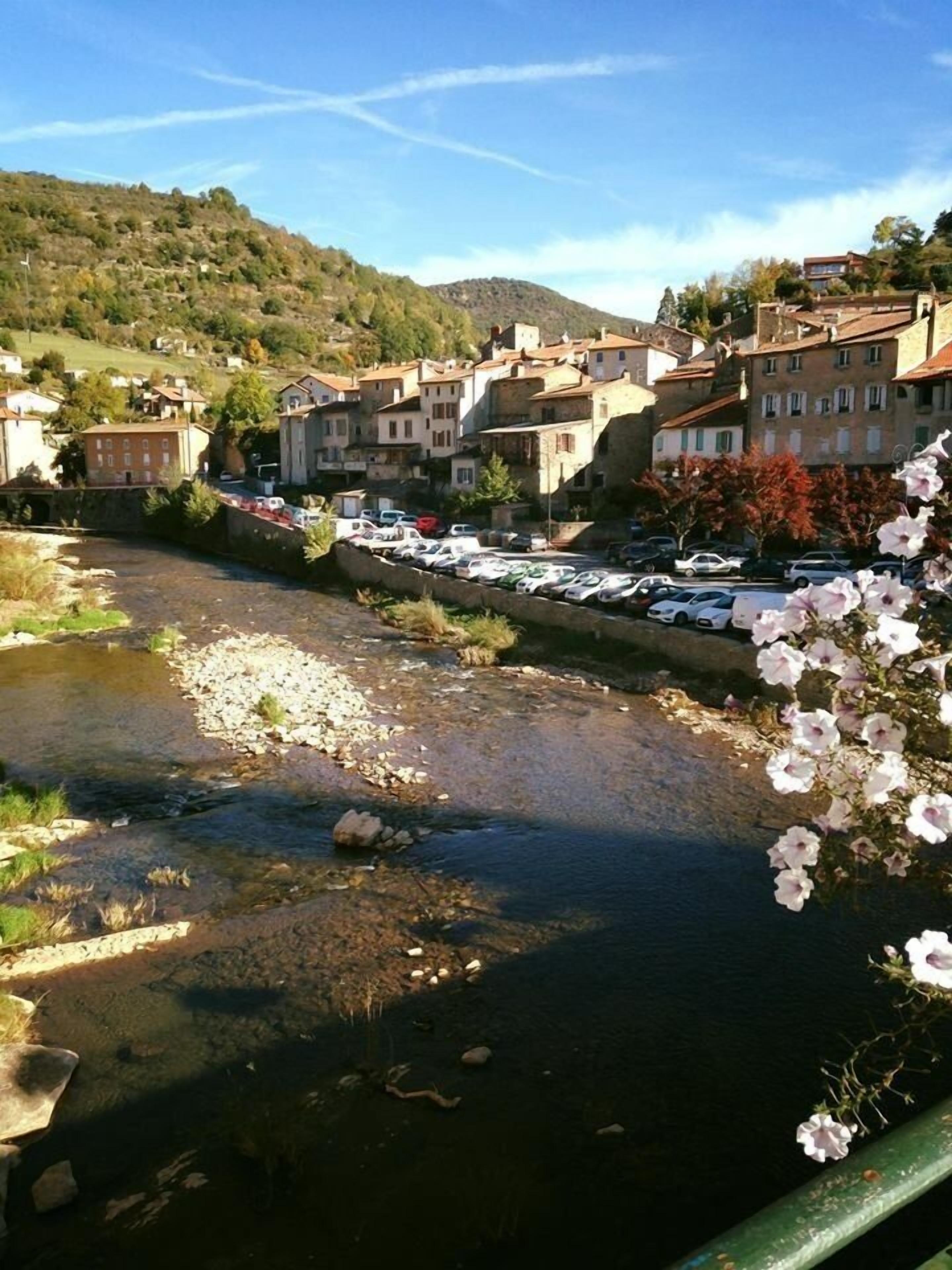 Un río con un puente, edificios al fondo y coches estacionados.