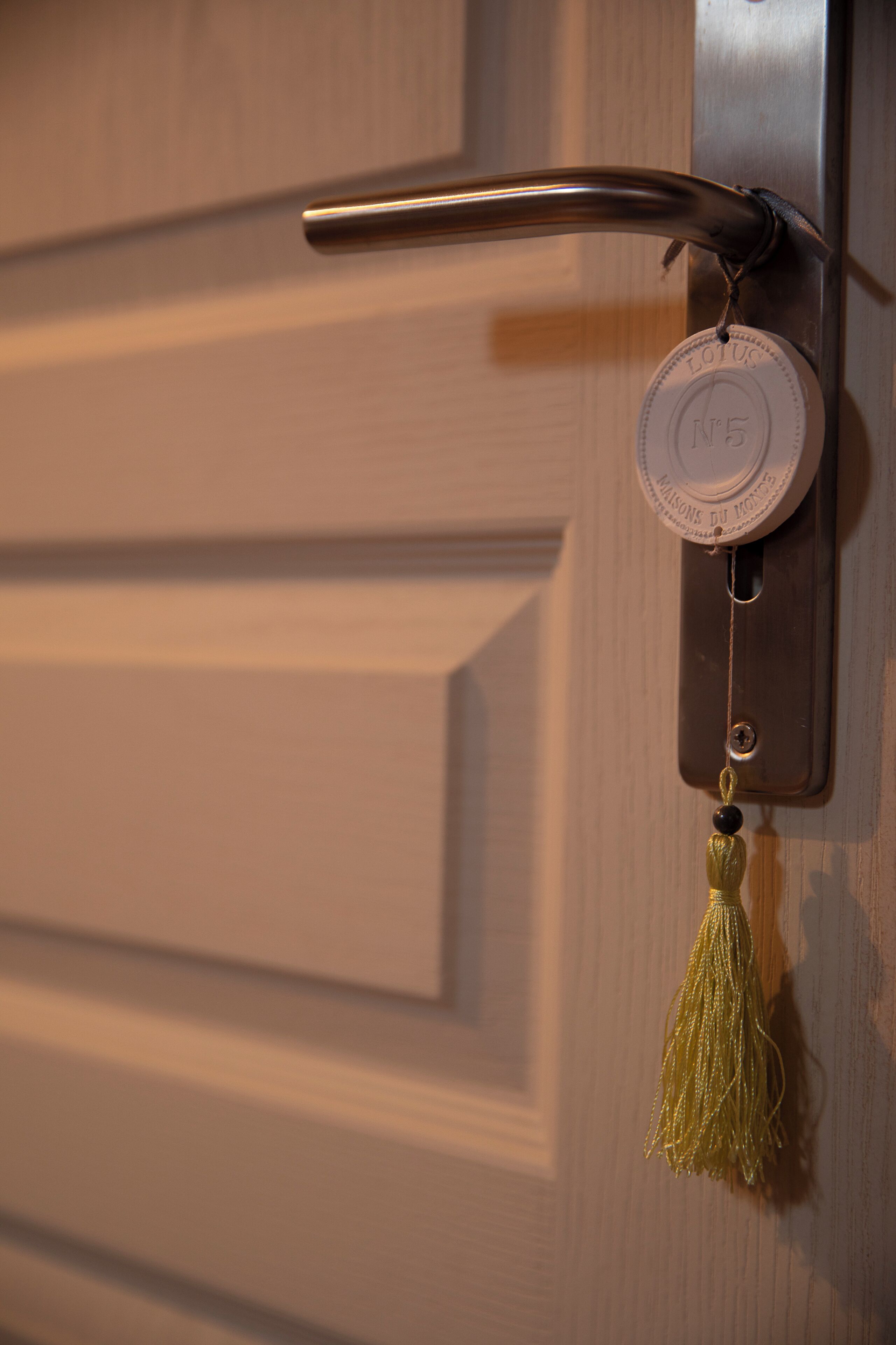 A door lock with a brass handle and a keyhole, a brass plate with a number, and a tassel hanging from the lock.