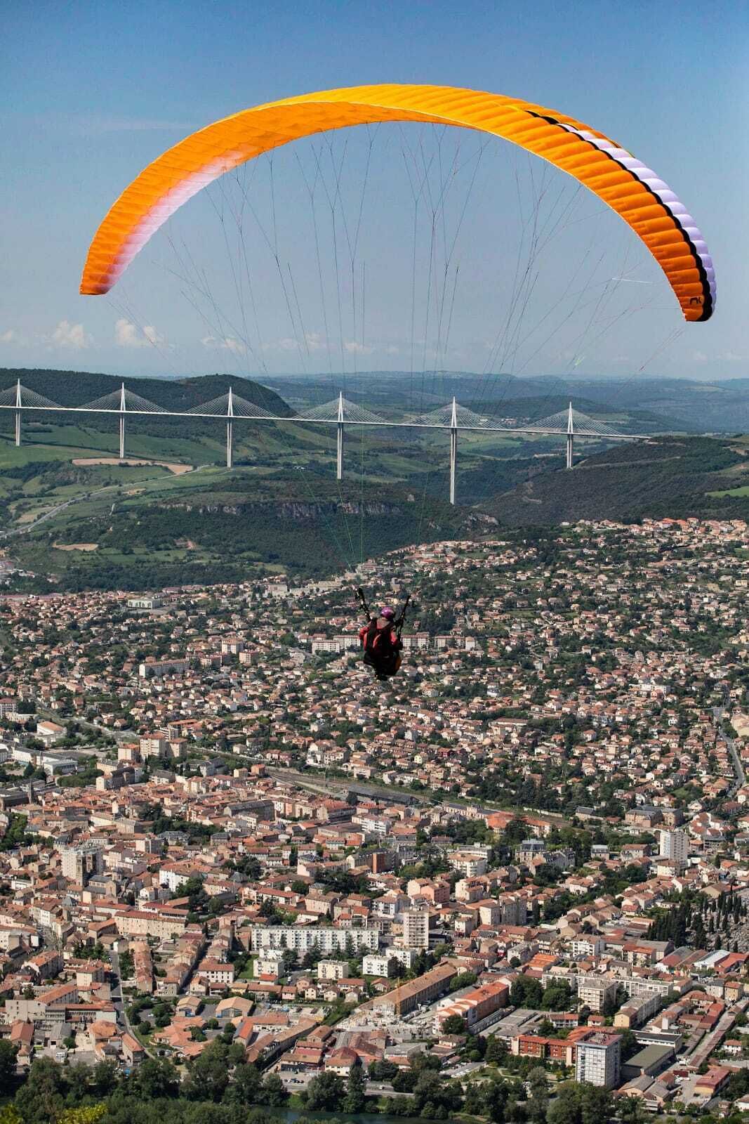 Een persoon hanggliding boven een dichtbevolkte stad, met een brug op de achtergrond.