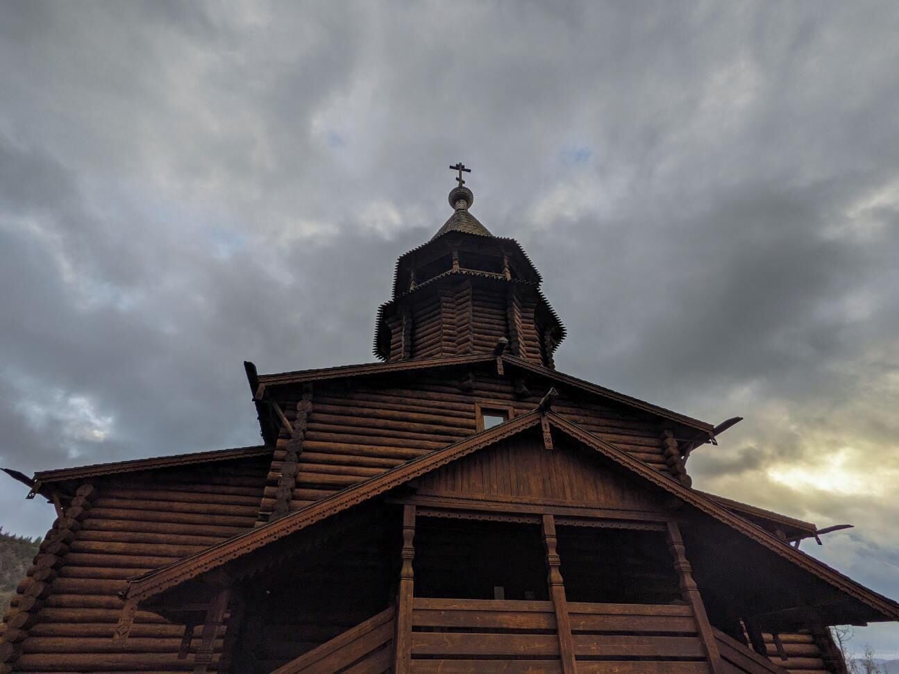 A wooden building with a prominent tower and cross on top, under a cloudy sky.