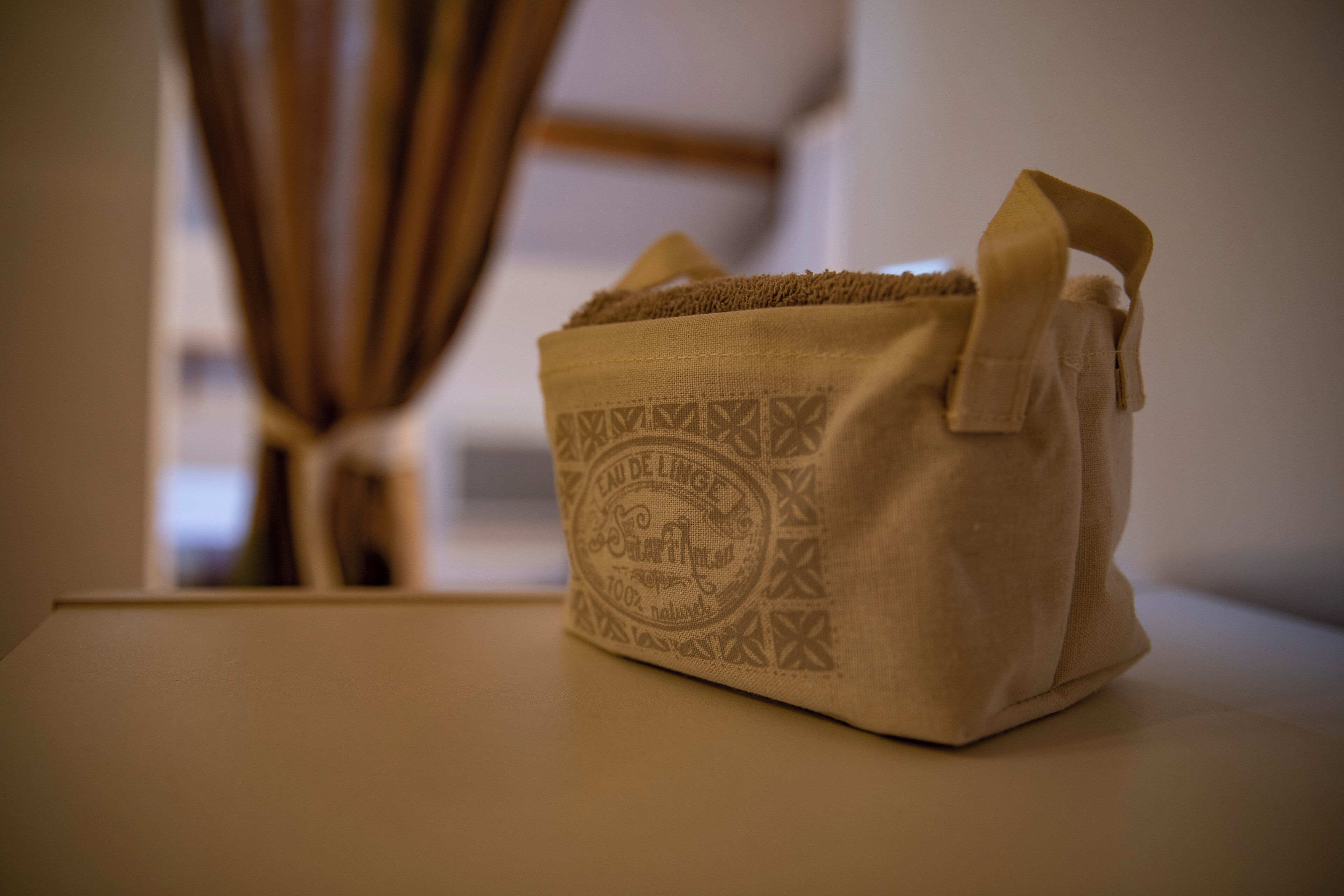 Een beige tas van stof met een handvat en een decoratief patroon, geplaatst op een vlak oppervlak.