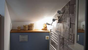 Une petite salle de bain avec des toilettes blanches, un lavabo et un miroir. On y trouve des paniers en osier accrochés au mur et un porte-serviettes.