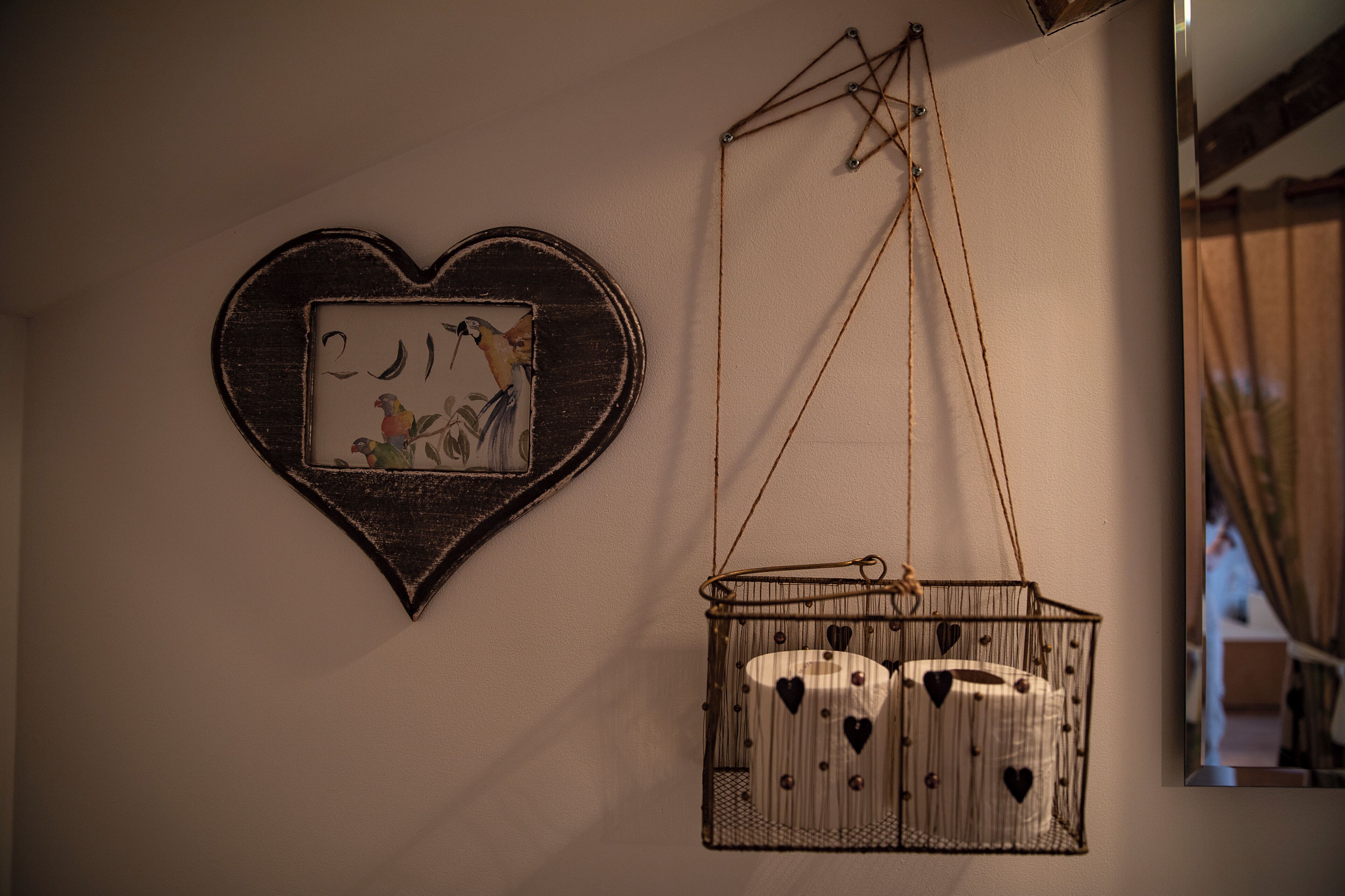 A wall with a heart-shaped decoration and a hanging birdcage with heart-shaped cutouts.