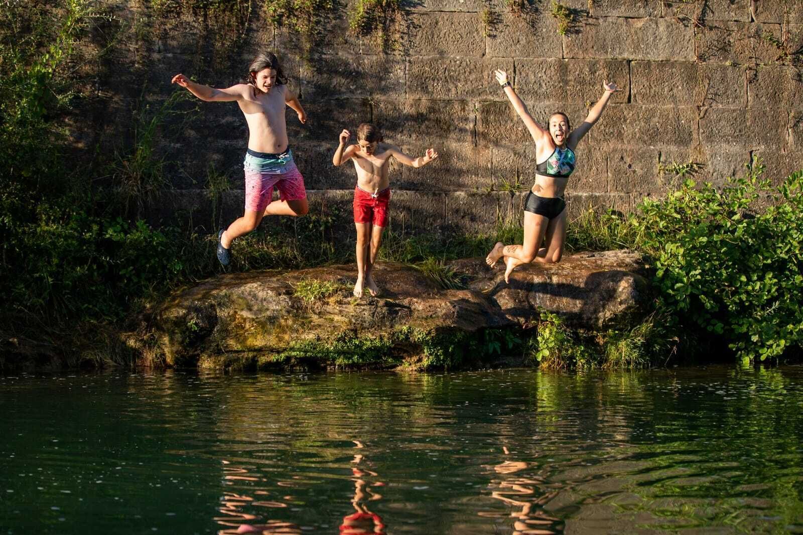 Three people jumping off a rock into a body of water.