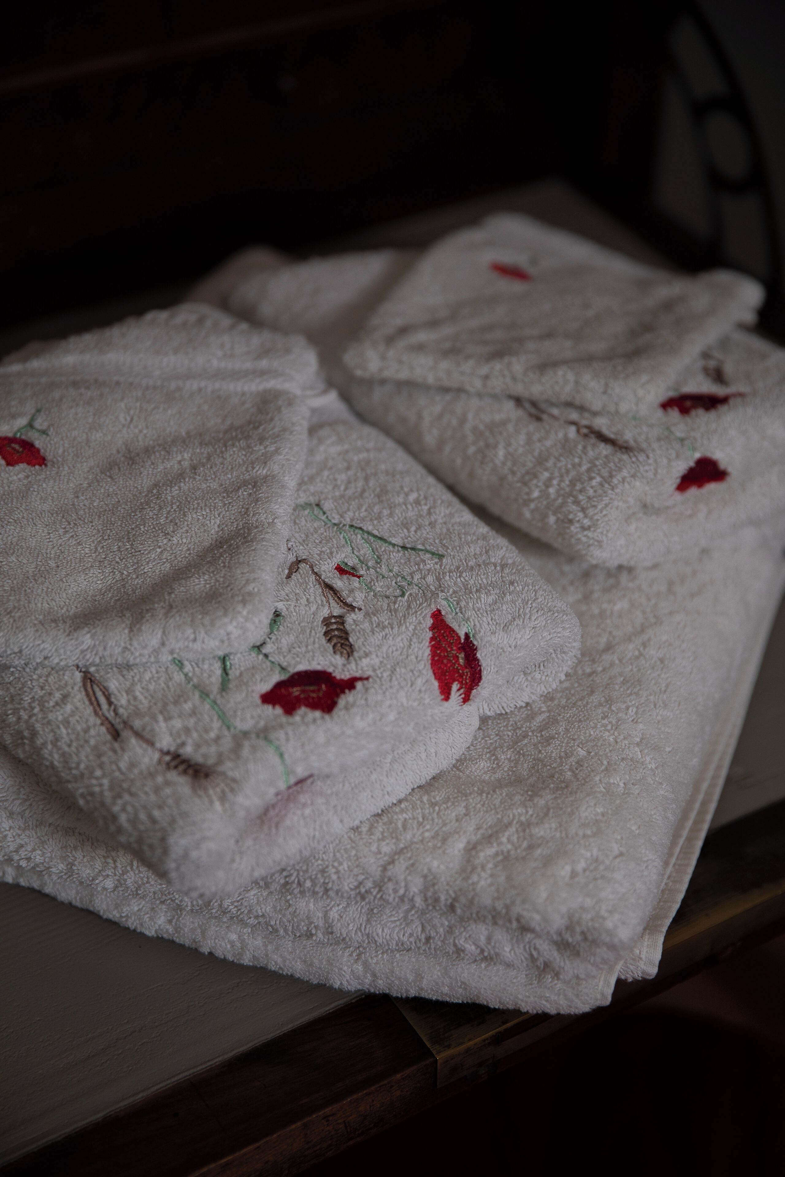 Une serviette blanche ornée de broderies florales rouges, posée sur une surface en bois.