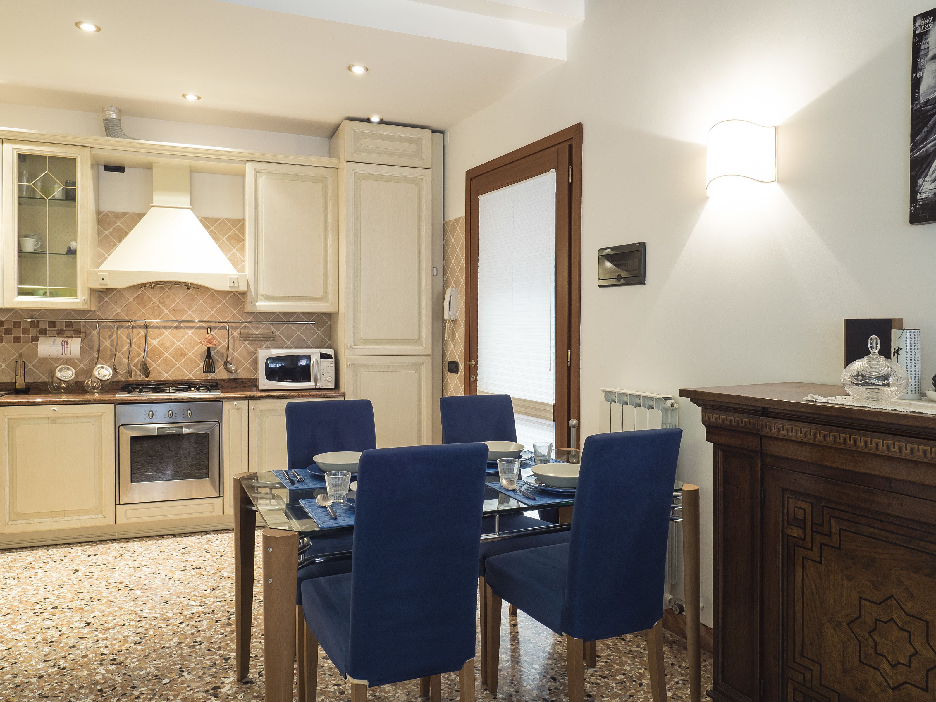 Una cocina moderna con armarios blancos, un microondas y un comedor con sillas azules y una mesa.