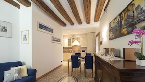 Una sala moderna con un sofá azul, una mesa de centro y una estrella decorativa en el suelo. Se observa una cocina al fondo con un comedor.