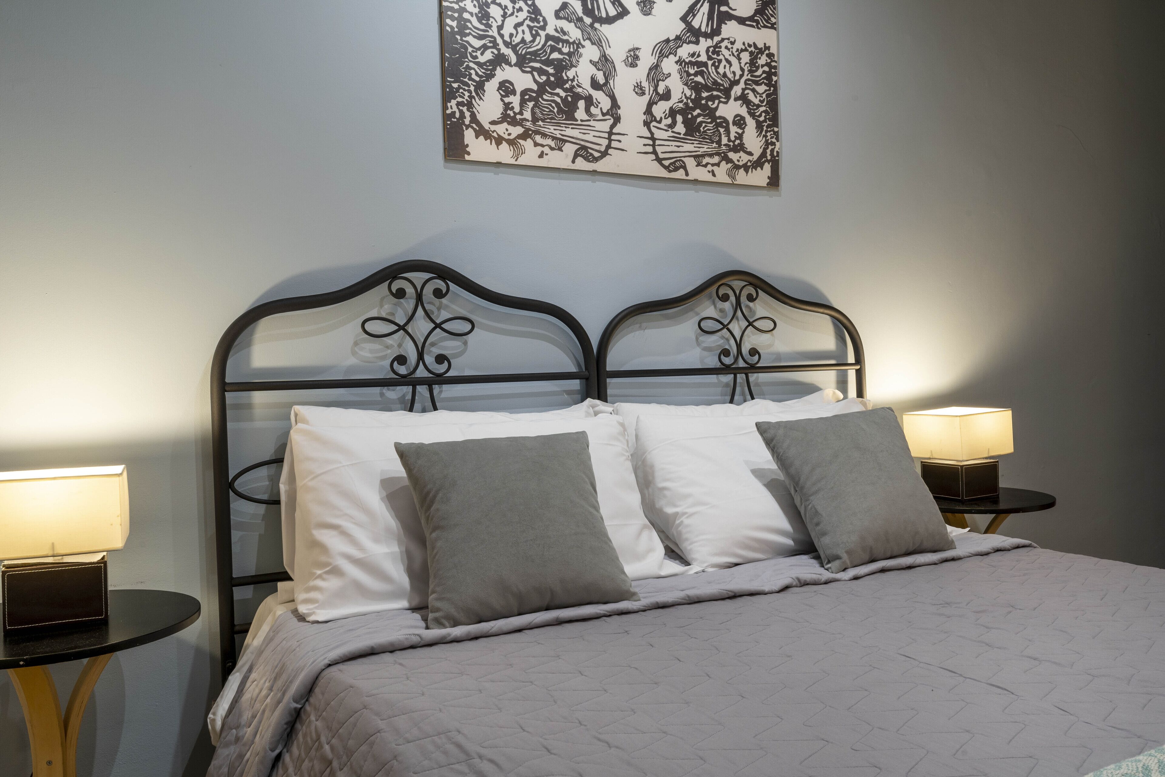 A neatly made bed with a quilted cover, two bedside tables with lamps, and a wall-mounted artwork above the bed.