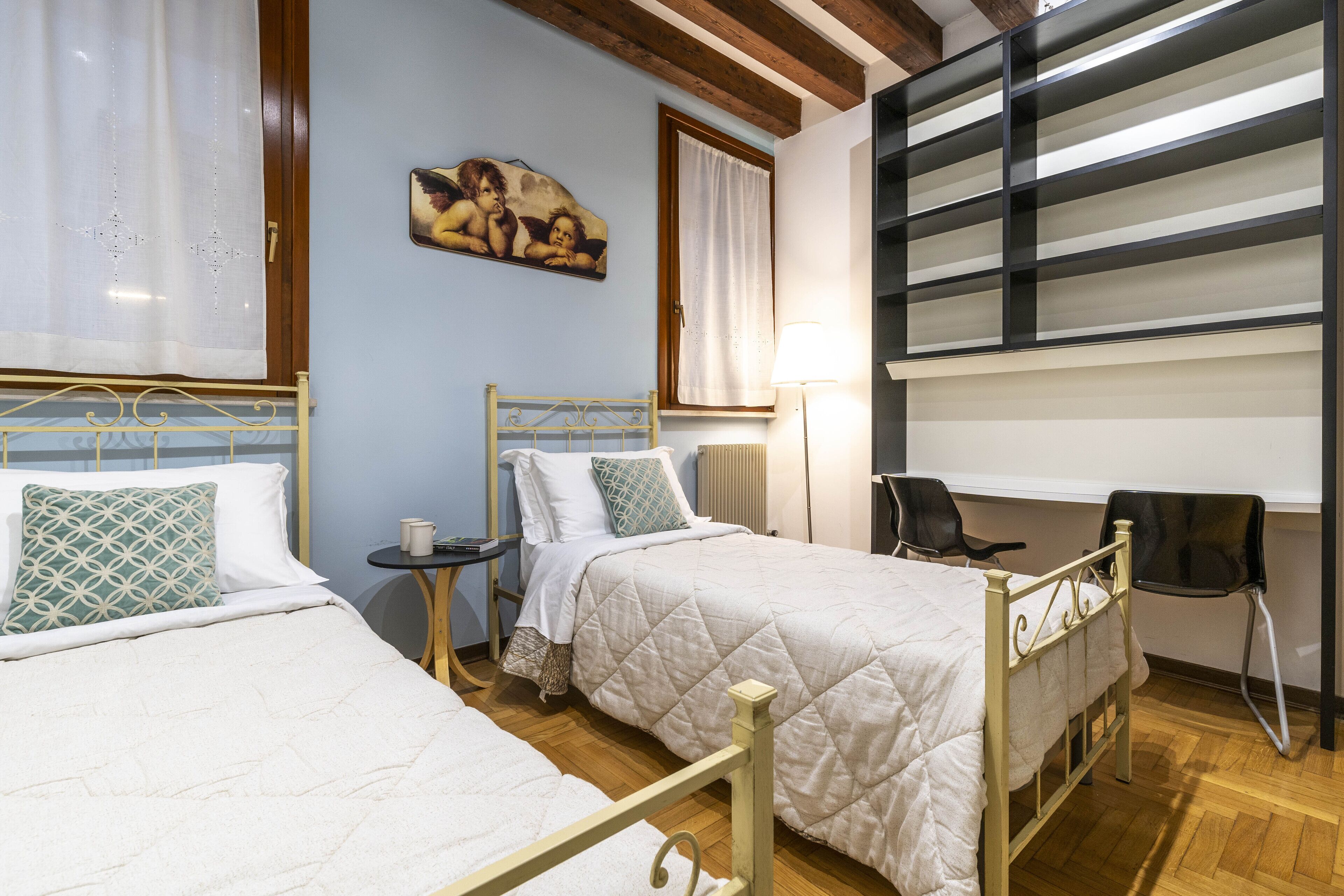 A hotel room with two beds, a desk, a chair, a lamp, and a painting on the wall.