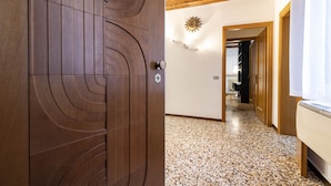 A wooden door with a circular design, a hallway with a speckled floor, and a wall-mounted light fixture. - San Moisé (Venice)
