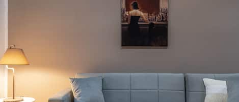 A modern living room with a grey sofa, a lamp, and a painting on the wall.