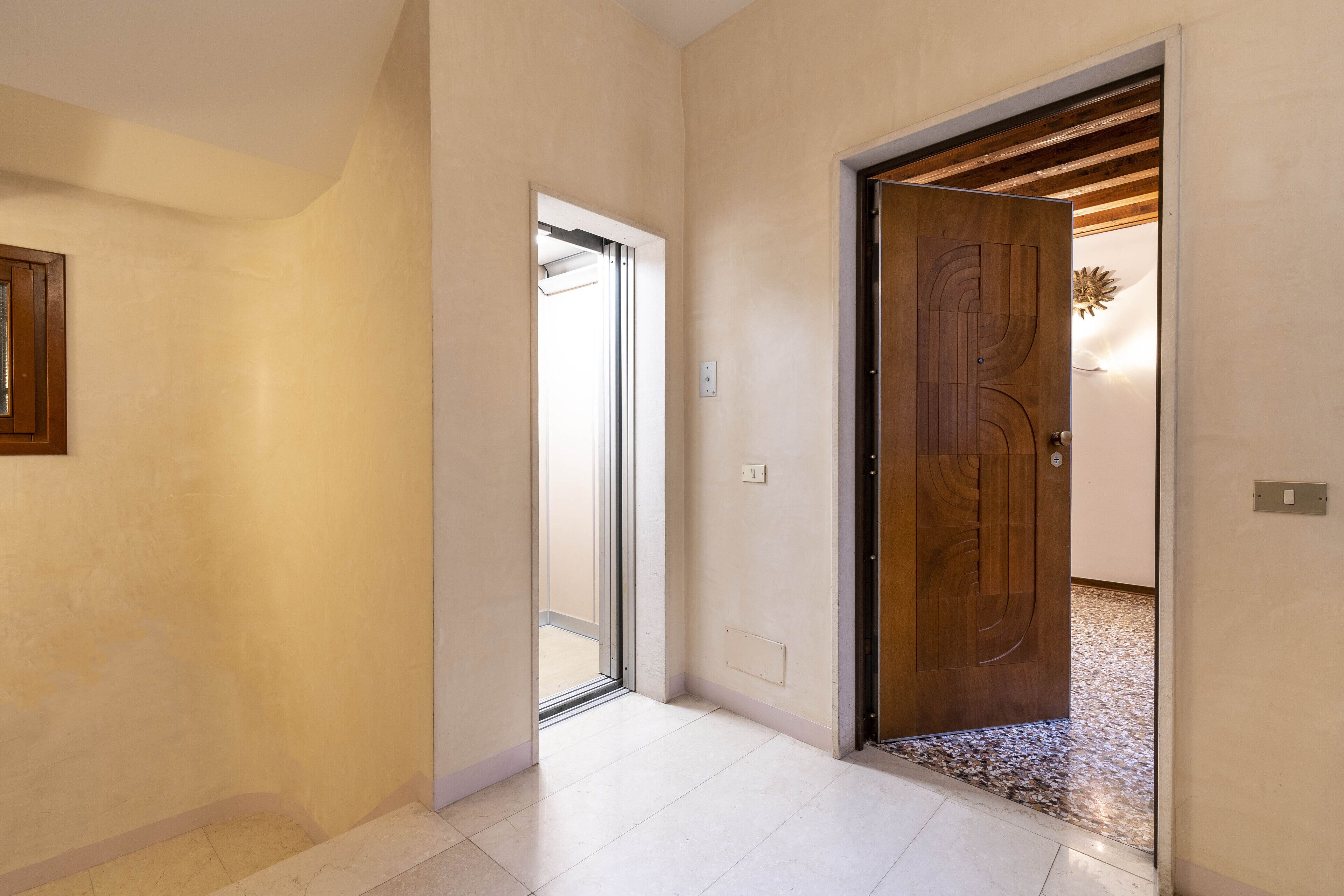 A hallway with a wooden door, a glass door, and a light switch on the wall.