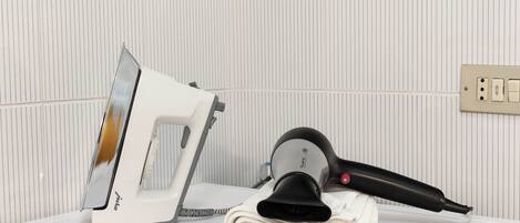 A bathroom with a white countertop, a white iron, a black hairdryer, and a towel.