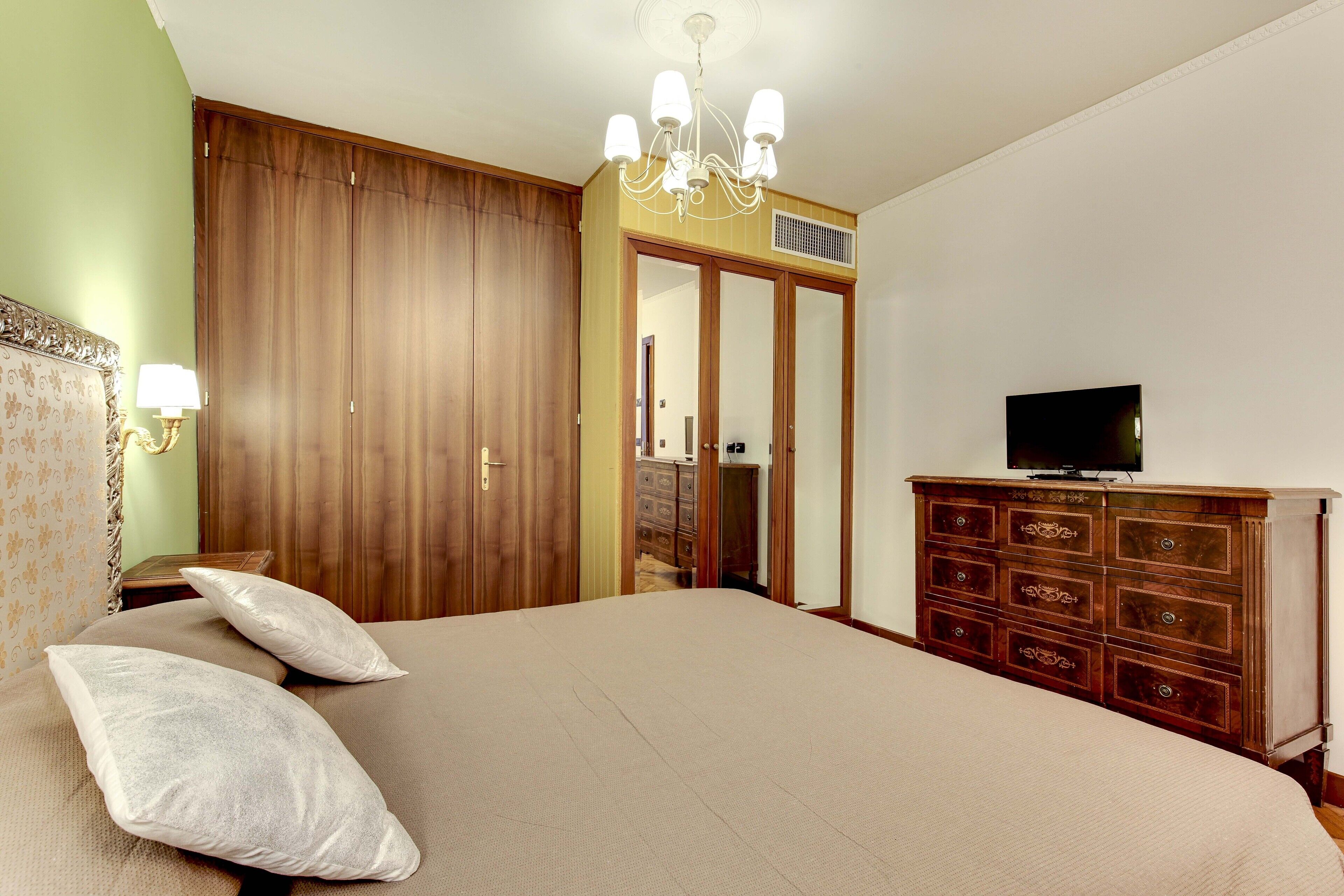 A bedroom with a large bed, wooden wardrobe, and a television on a dresser.