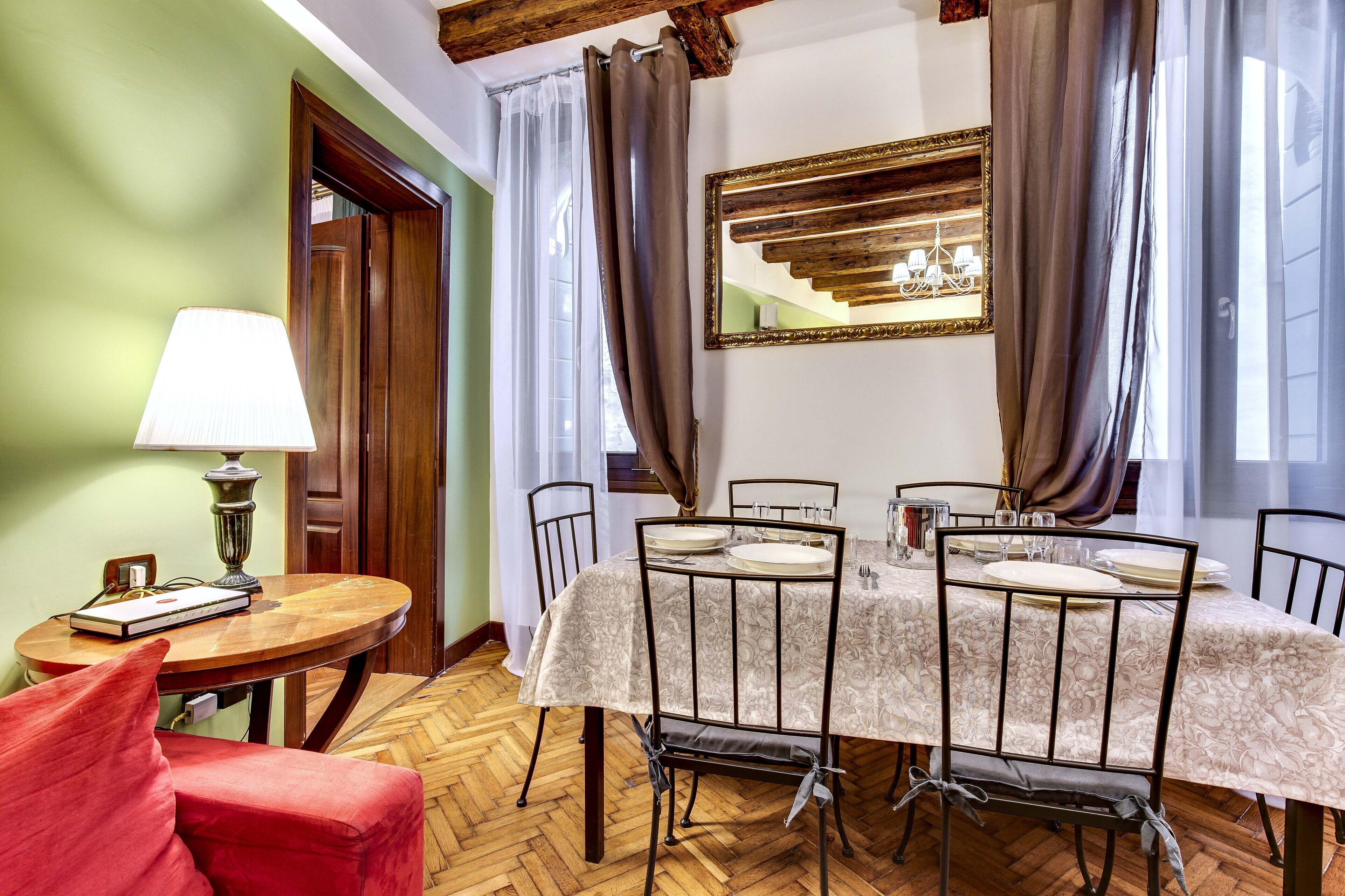 A dining area with a table set for six, surrounded by chairs, a lamp, and a red chair.