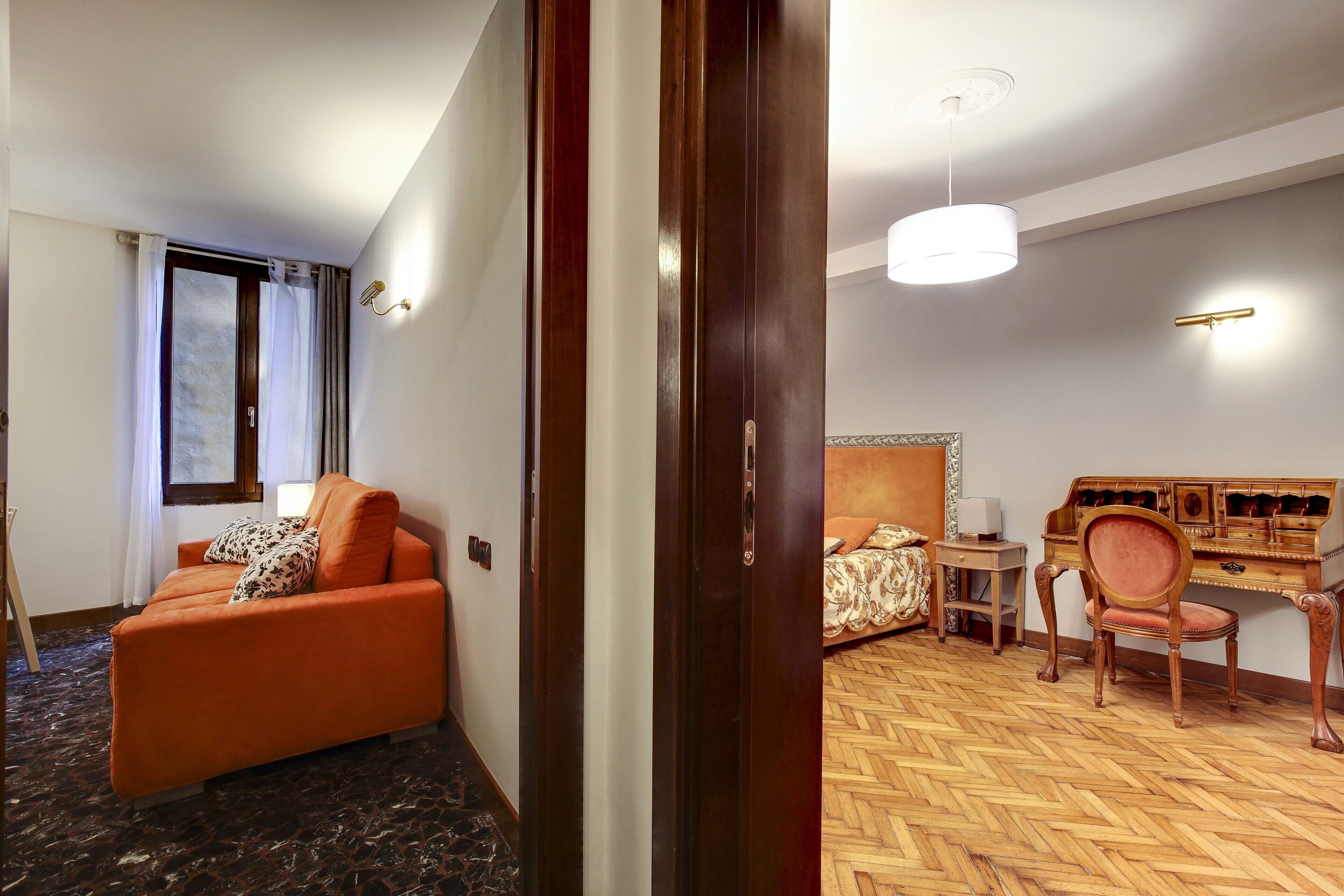 Una camera d'albergo con pavimento in legno, un divano, un letto, una scrivania e una sedia.