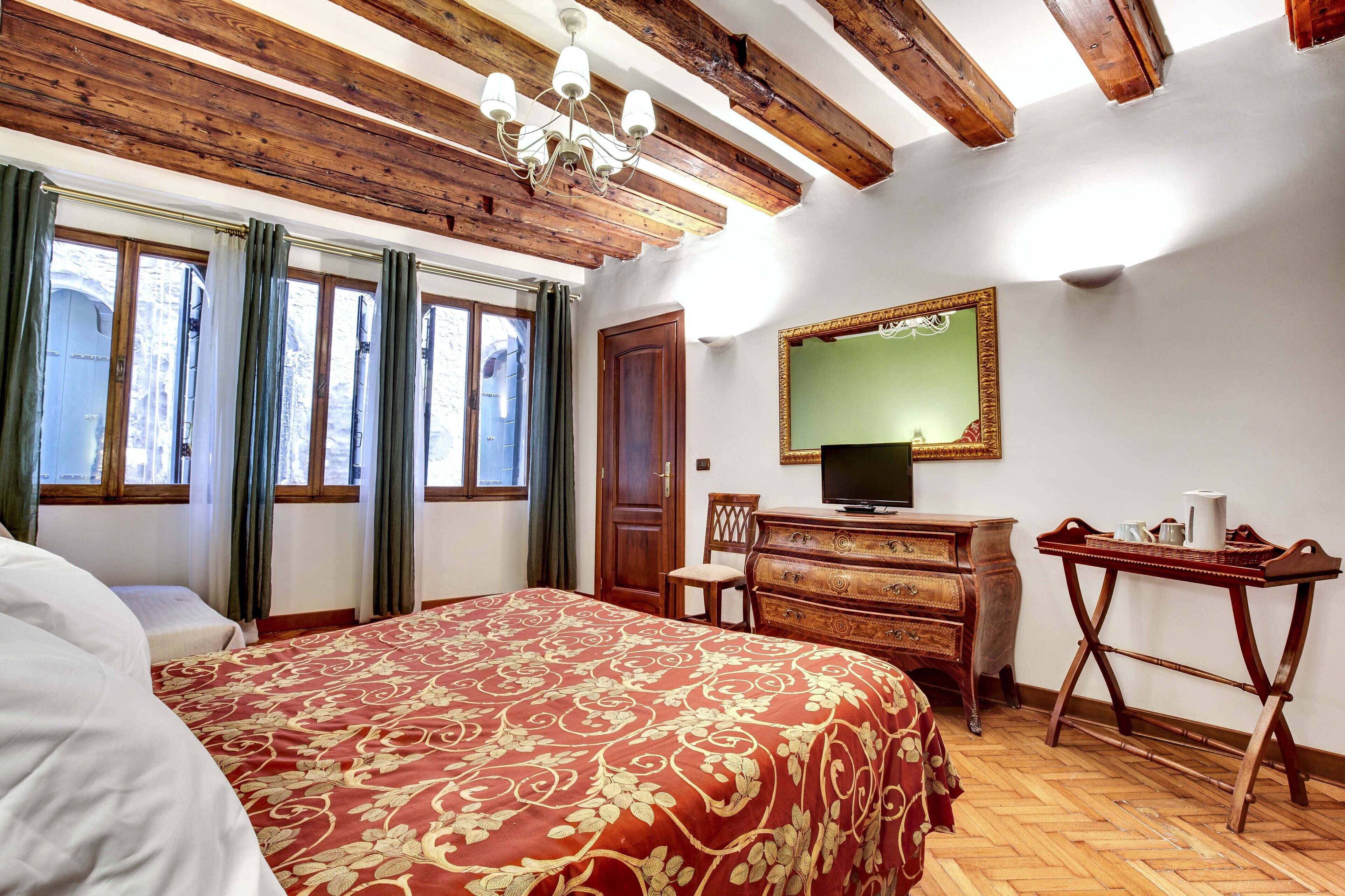 A bedroom with a large bed, wooden ceiling beams, a dresser, a mirror, and a television.
