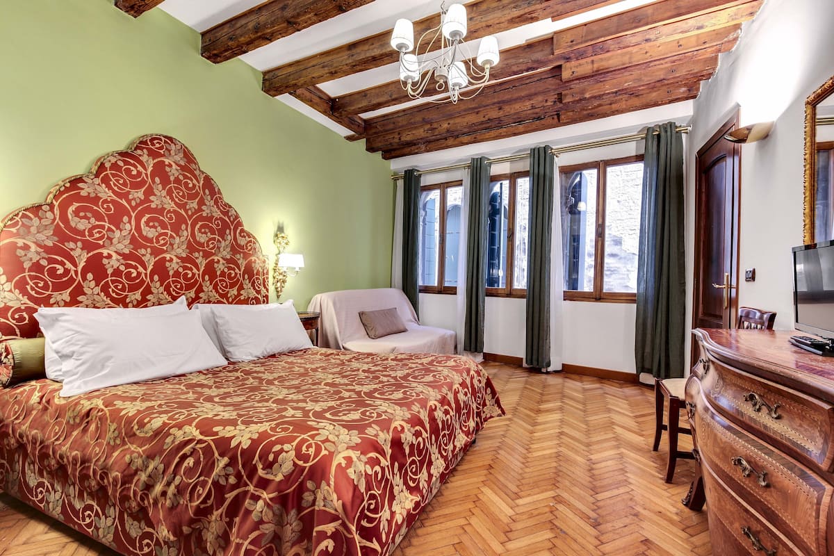 Ein Hotelzimmer mit einem großen Bett, Holzbalkendecke, einem Schminktisch und einem Fernseher.
