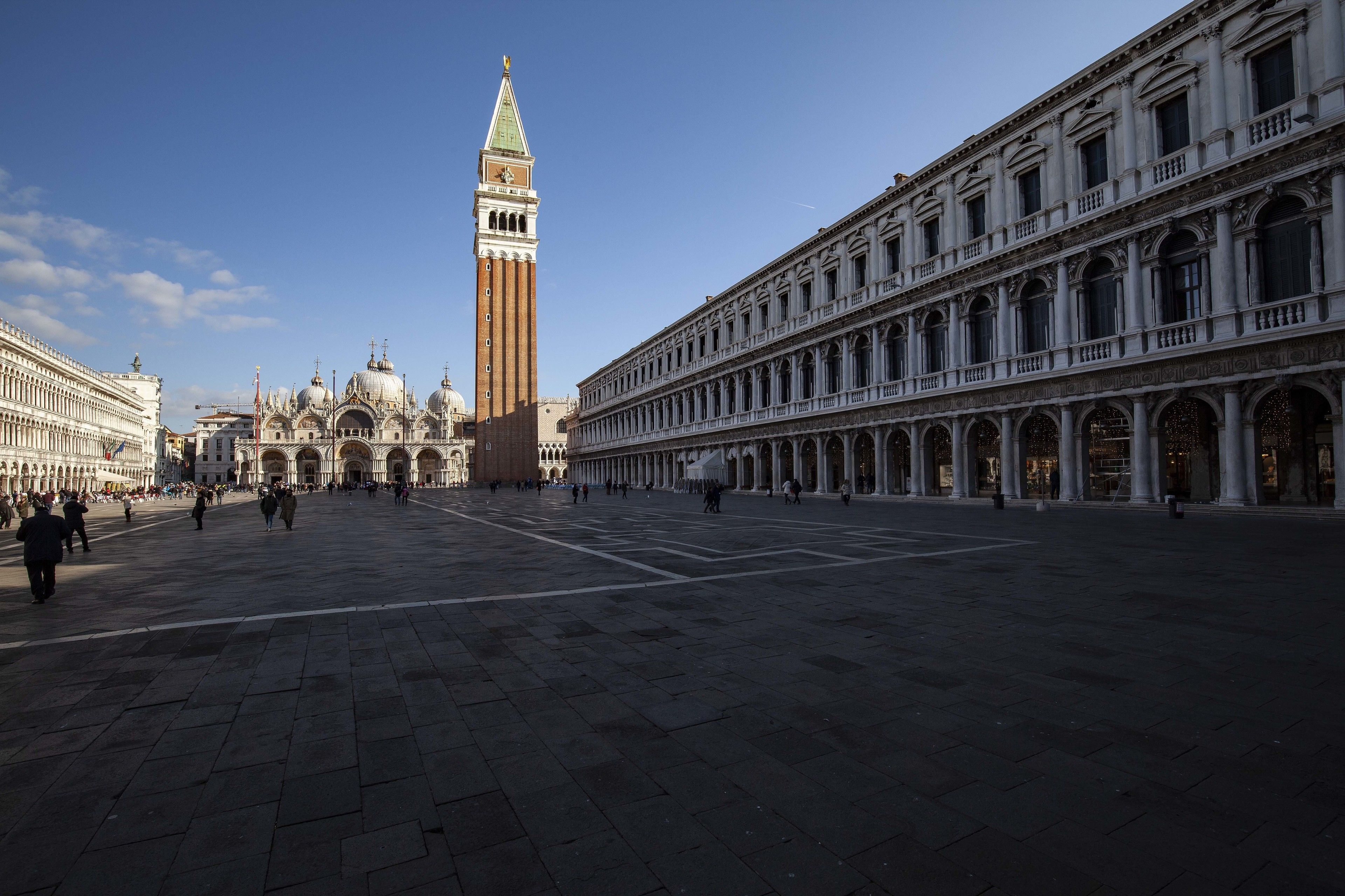 A spacious square with historic buildings, including a prominent tower and a long covered walkway.