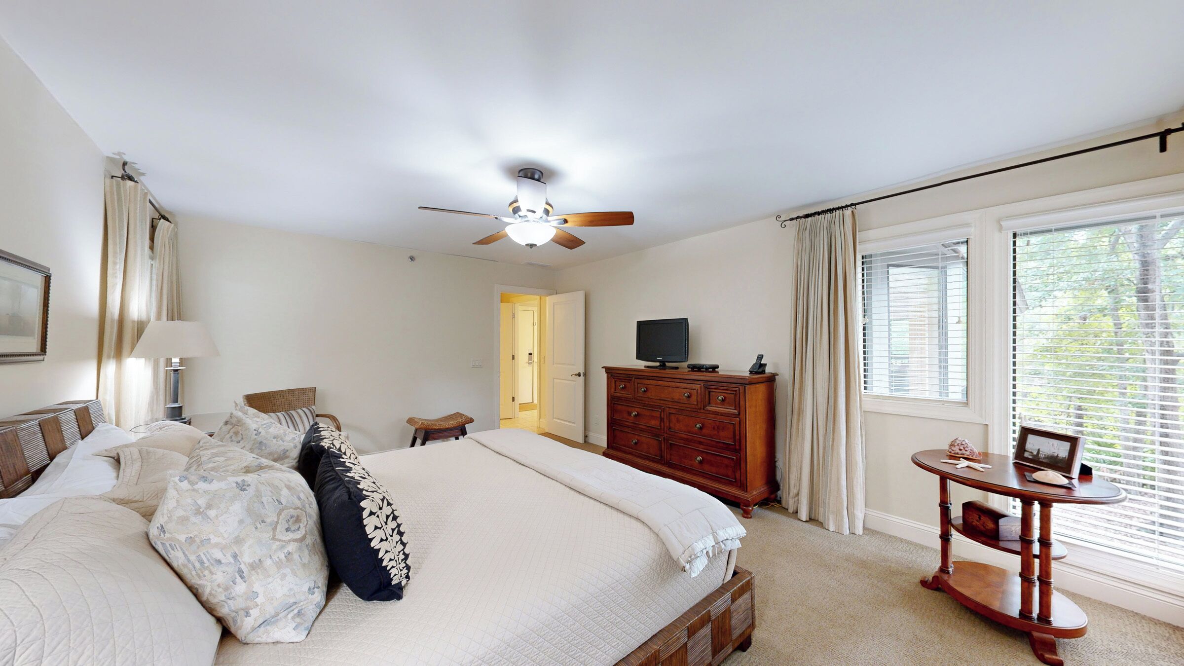 A bedroom with a bed, a dresser, a television, a desk, and a window with blinds.