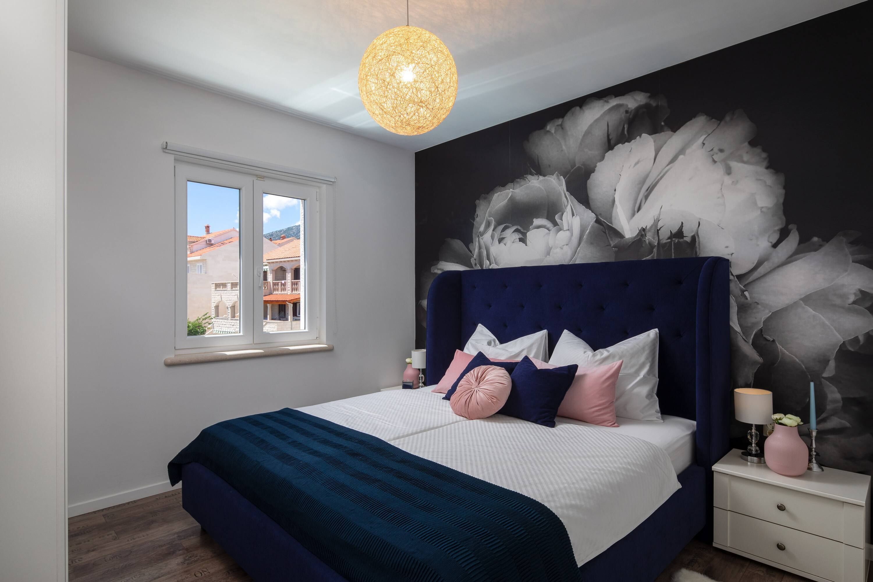 A bedroom with a large bed, a window, a wall mural, and a hanging light fixture.