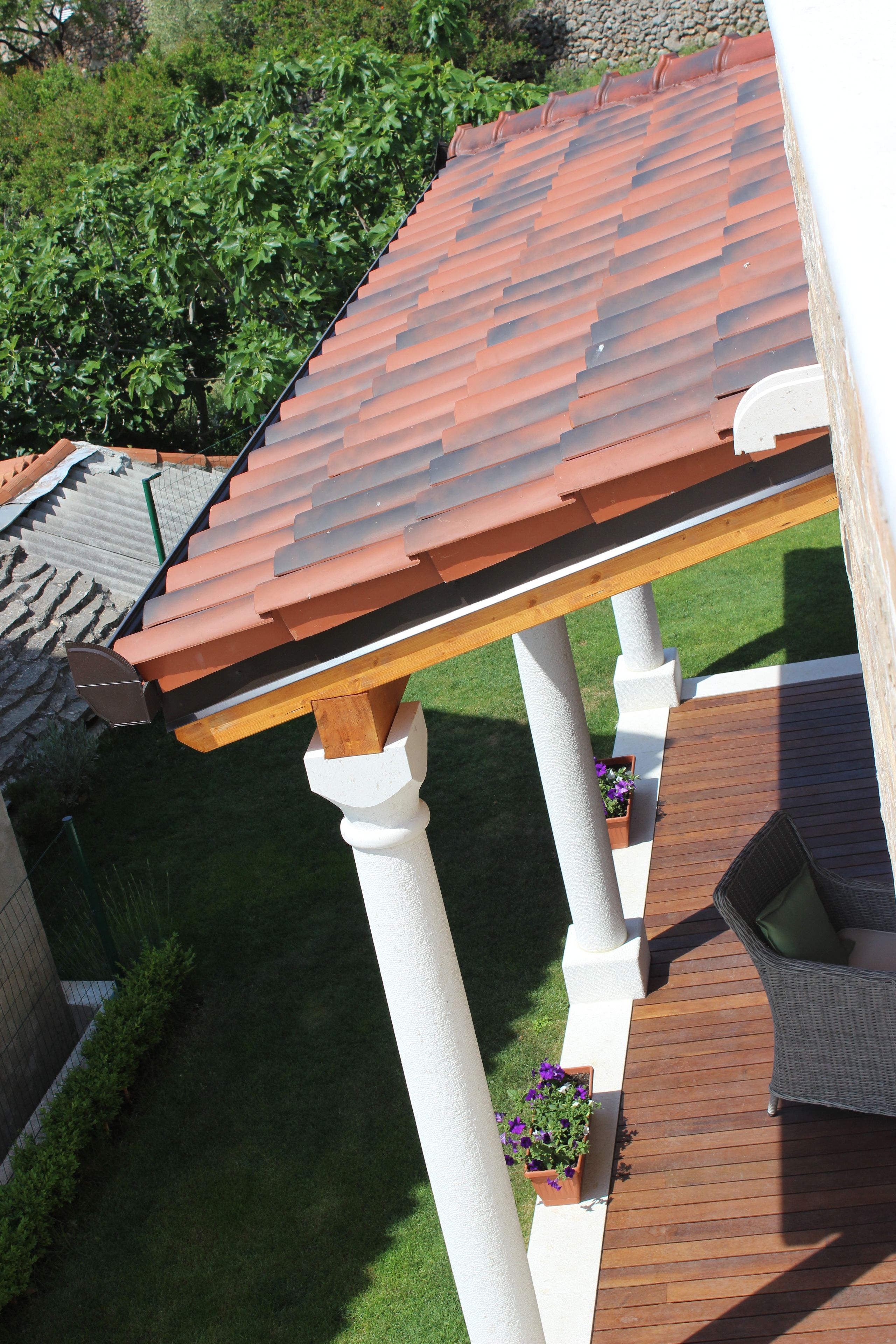 A rooftop patio with a wooden pergola, potted plants, and a wicker chair.