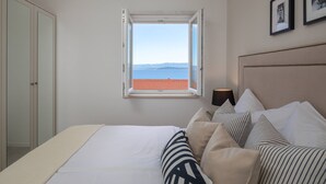 A bedroom with a bed, pillows, a nightstand, a lamp, a window with a view of the sea, and a wardrobe. - Villa Valentina (Bol)