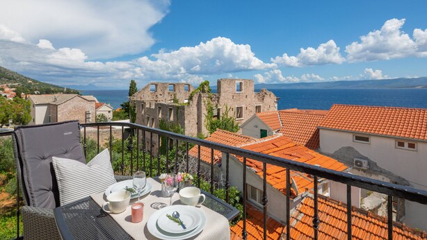 A balcony with a table set for two, overlooking a historic building and the sea. - Villa Valentina (Bol)