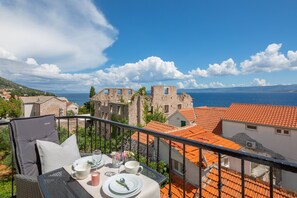 Varanda com mesa posta para dois, com vista para um edifício histórico e para o mar.