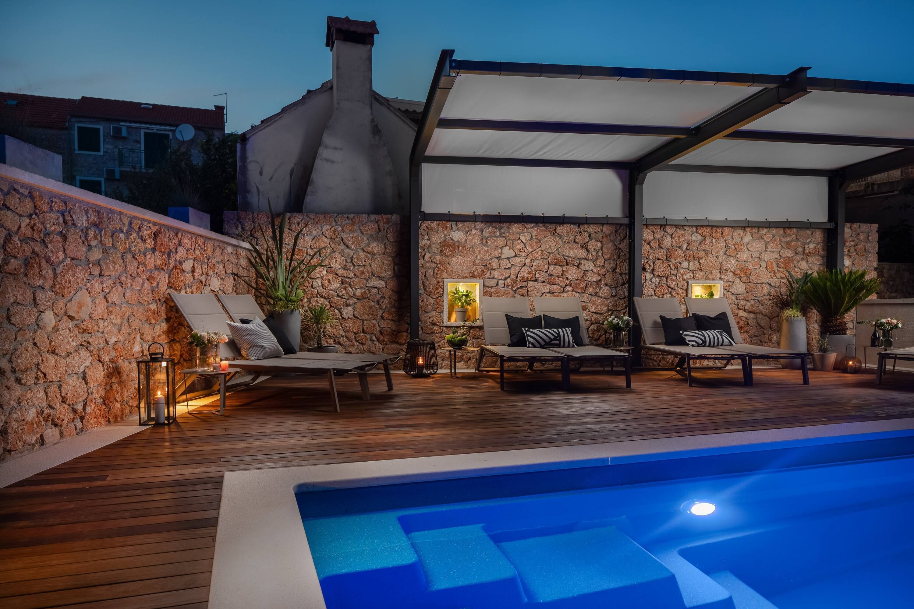 Uma área à beira da piscina com paredes de pedra, espreguiçadeiras e um espaço de estar coberto.