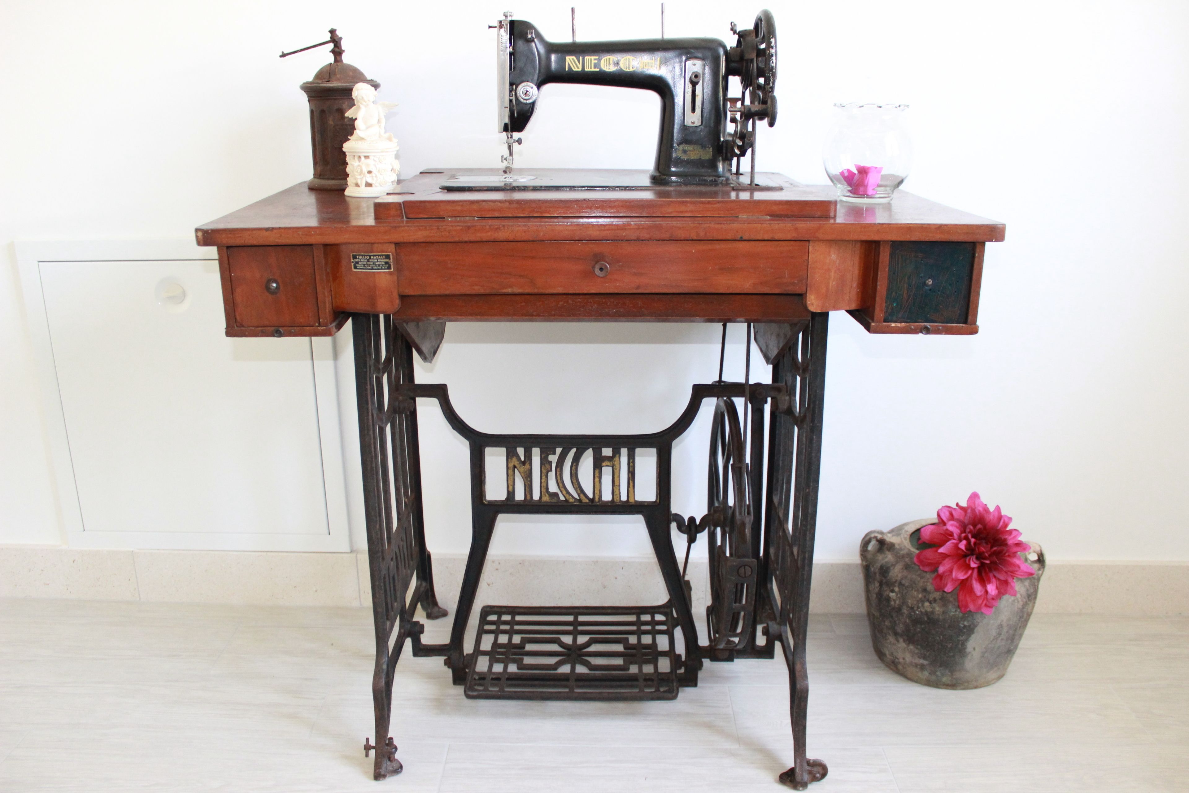 A vintage sewing machine on a wooden table with a small vase of flowers.