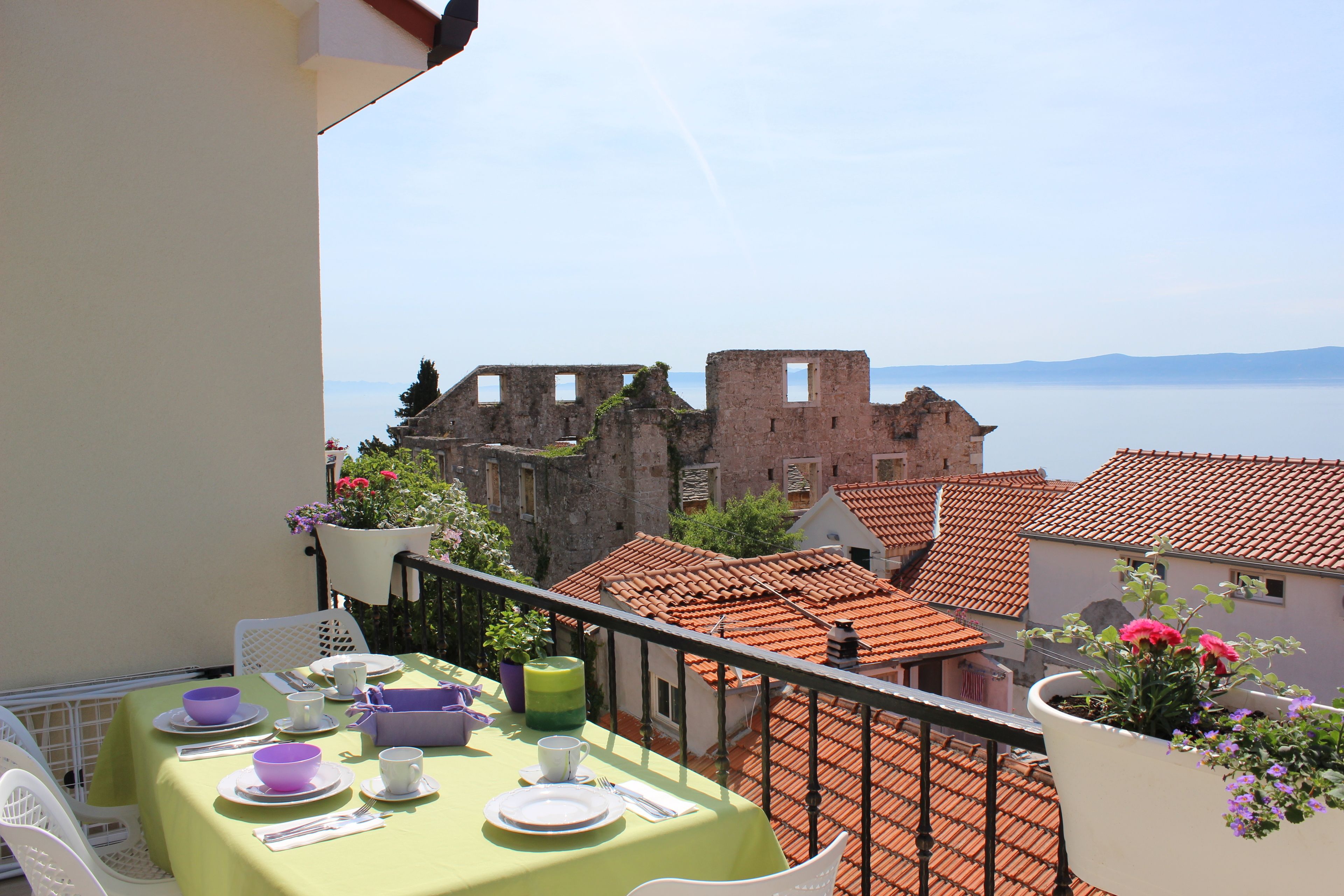 A balcony with a table set for a meal, overlooking a historic building and a body of water.