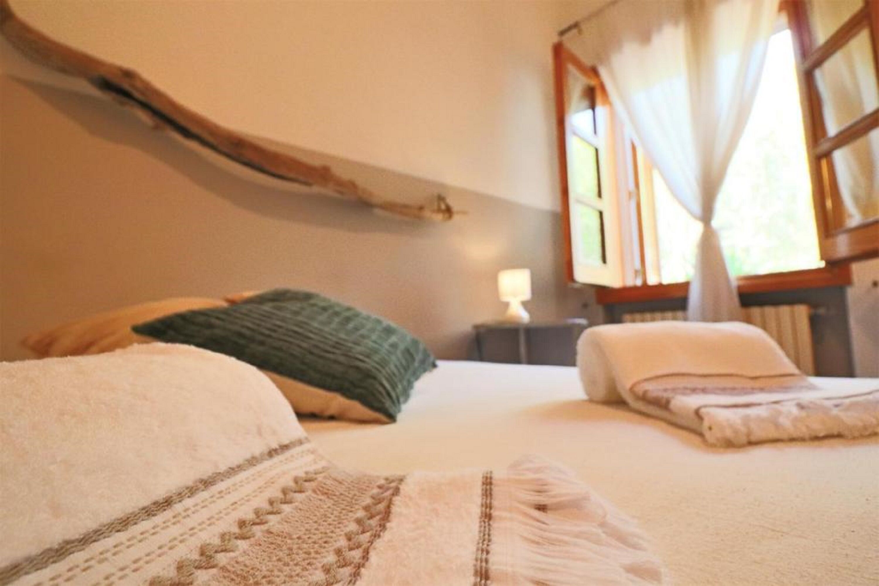 Une chambre à coucher avec un lit, des oreillers, une table de chevet et une fenêtre avec des rideaux.