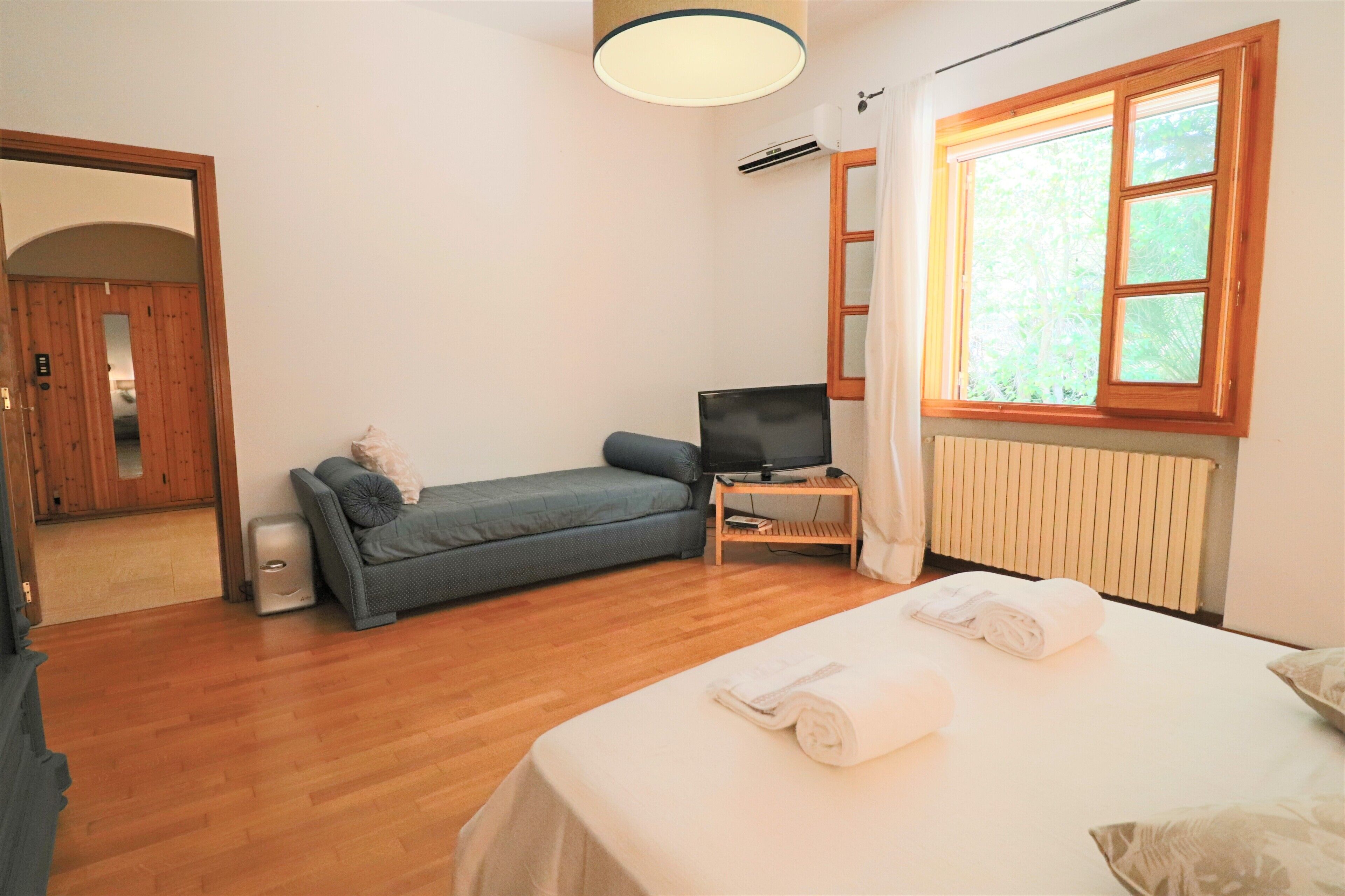 Una habitació amb un llit, un sofà, una televisió i una finestra amb cortines.