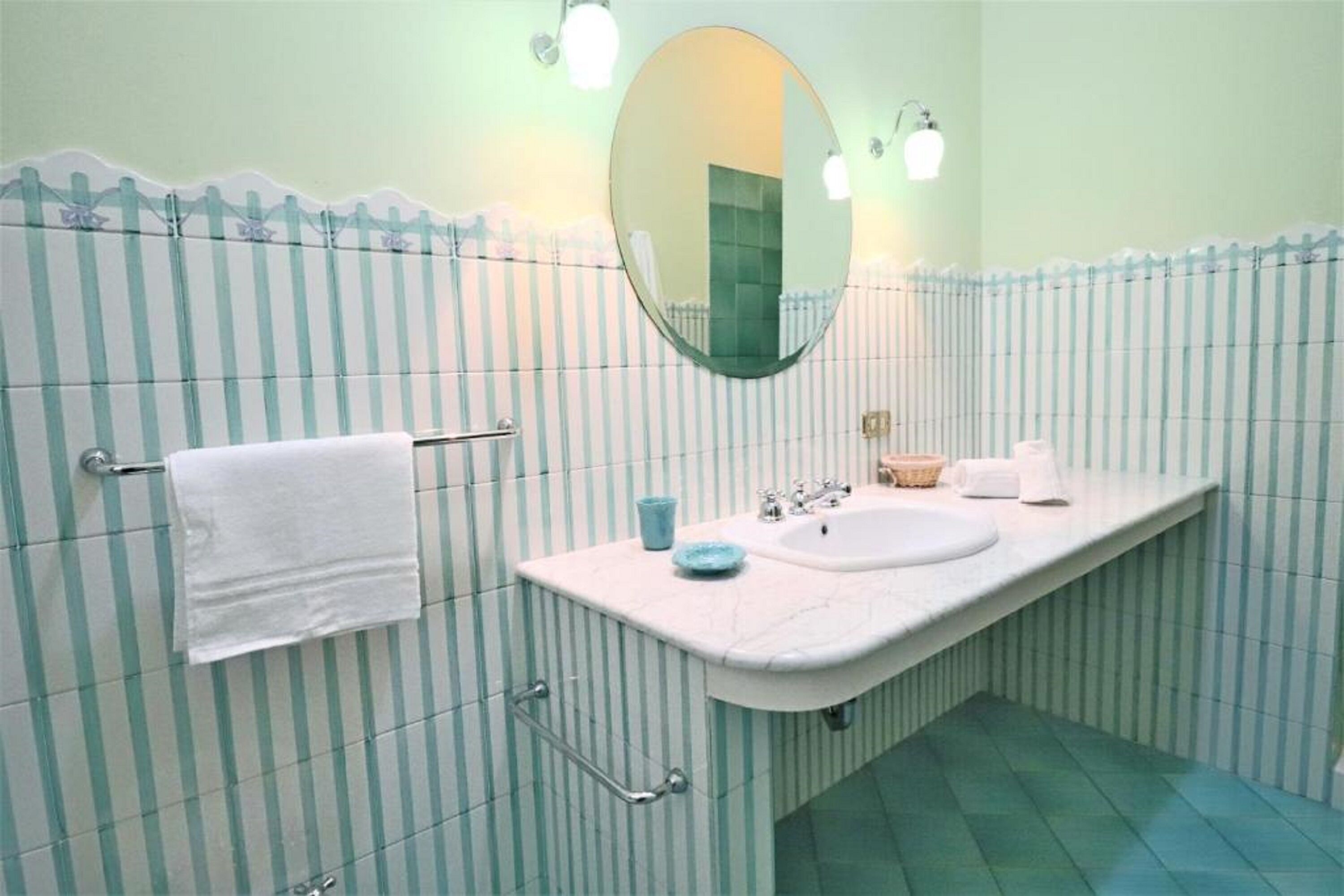 Ein Badezimmer mit gestreifter Wandgestaltung, einem weißen Waschbecken, einem Spiegel und einem Handtuchhalter.
