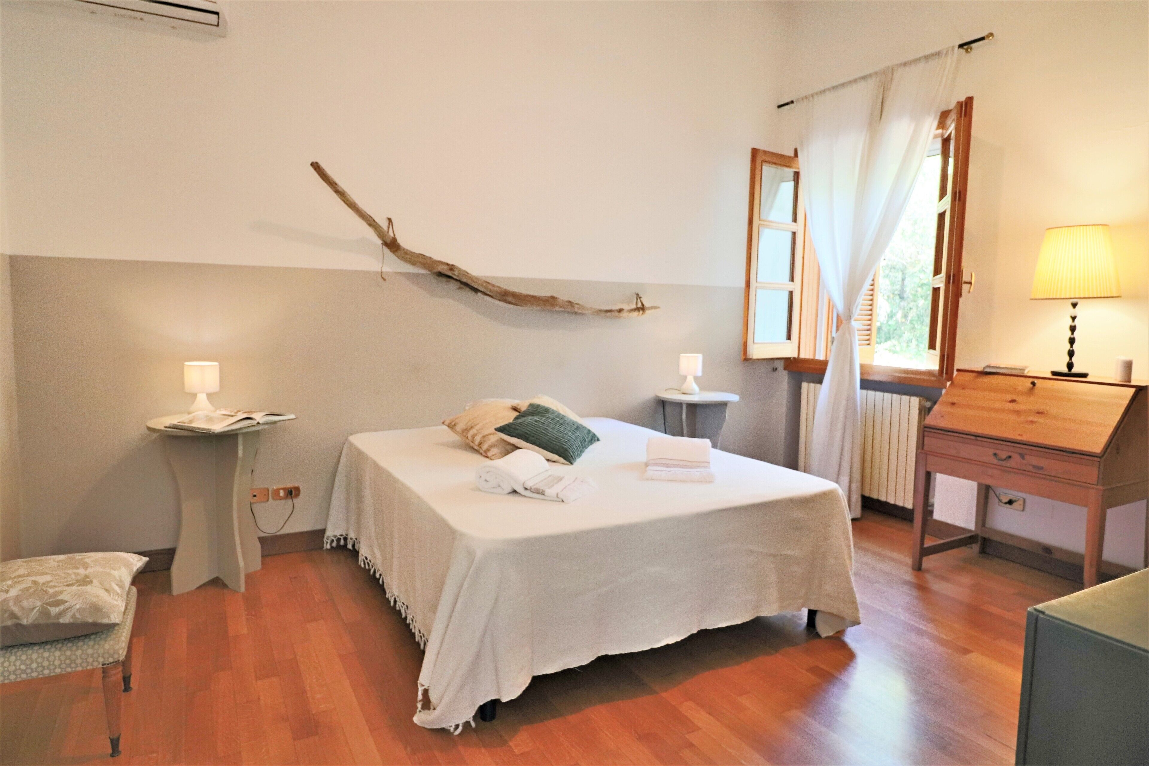 A bedroom with a bed, bedside tables, a lamp, a wooden desk, and a window with curtains.