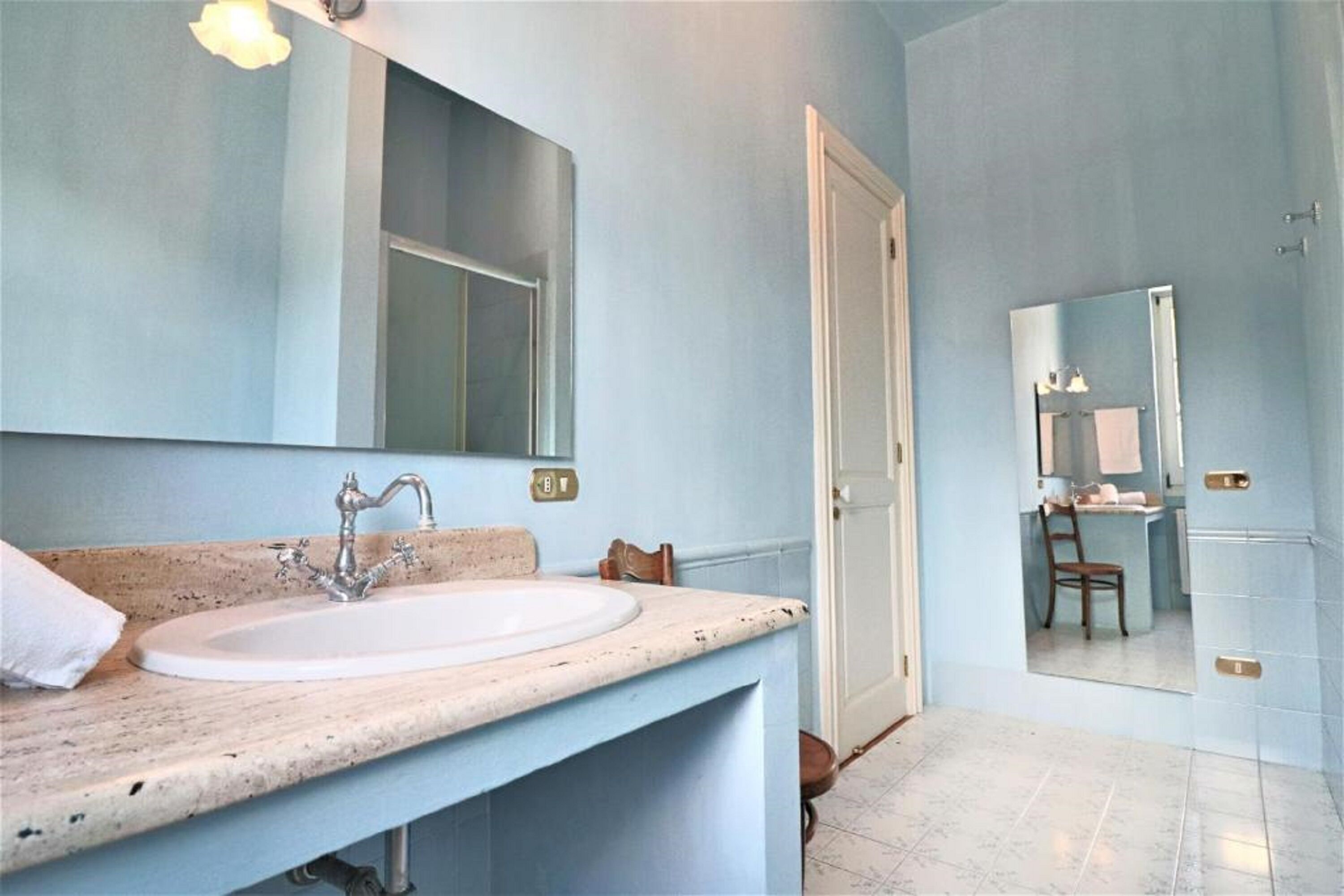 A bathroom with a sink, mirror, and door leading to another room.